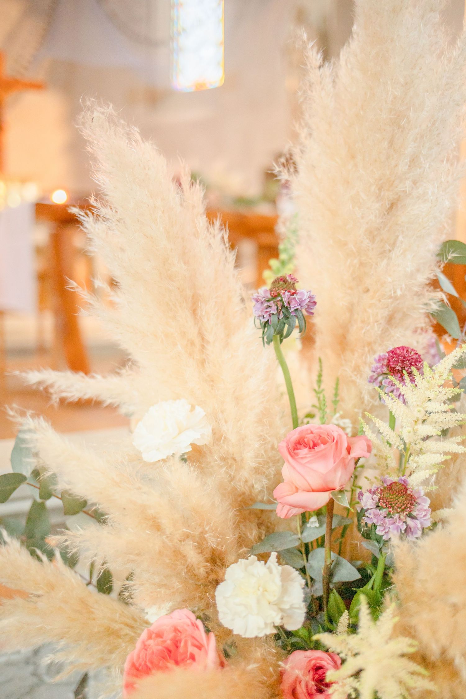 Elegant wedding flower arrangement featuring pampas grass and pink roses in soft focus.