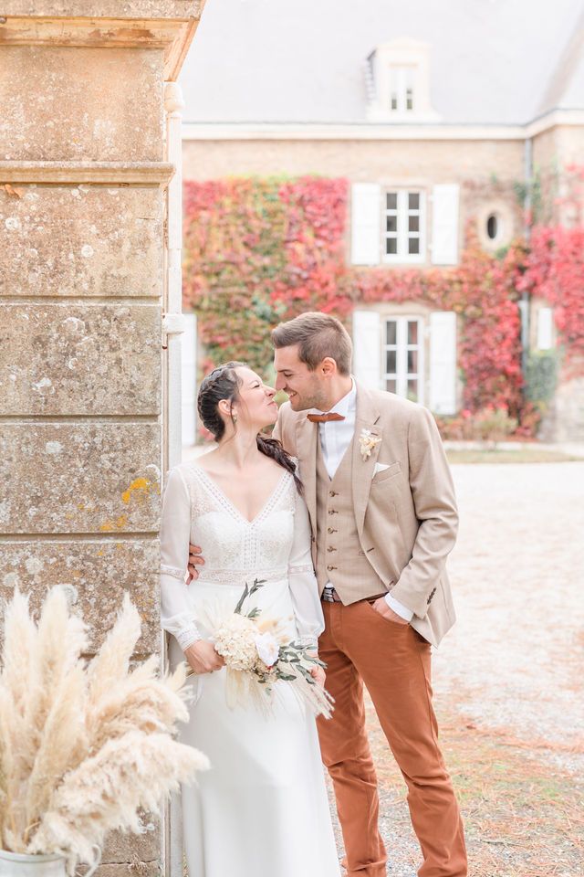 Elegant bride in white dress and groom in beige suit sharing intimate moments by garden columns.