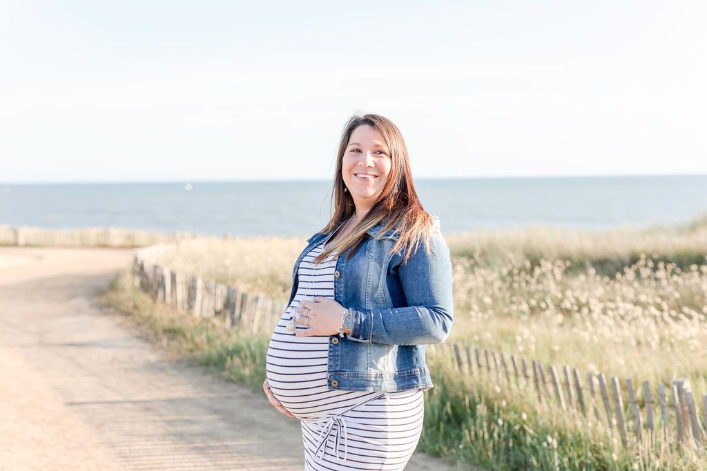 Joyful beach maternity portrait with striped dress and denim jacket.