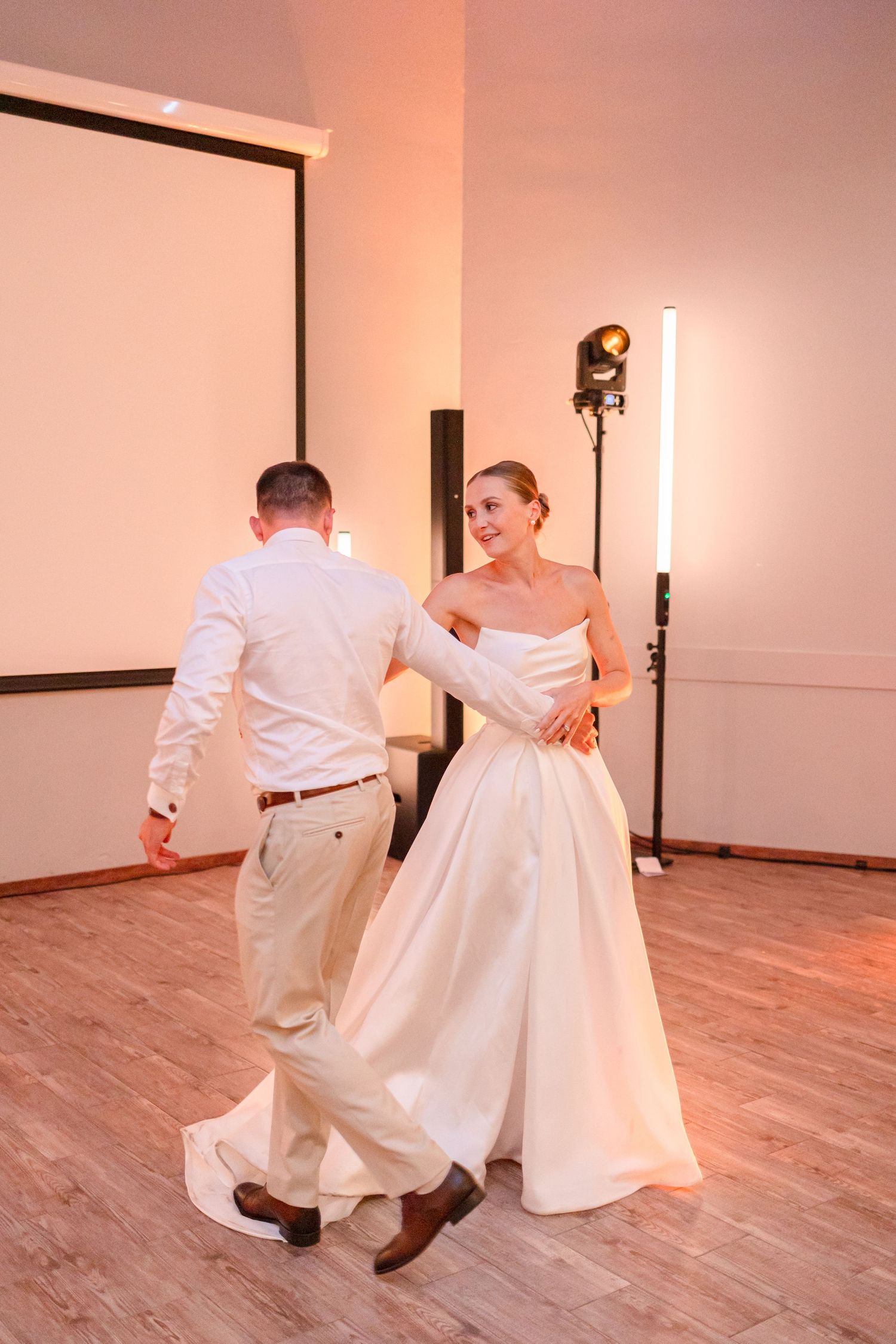 Couple dances on hardwood floor with white projection screen and professional lighting visible.
