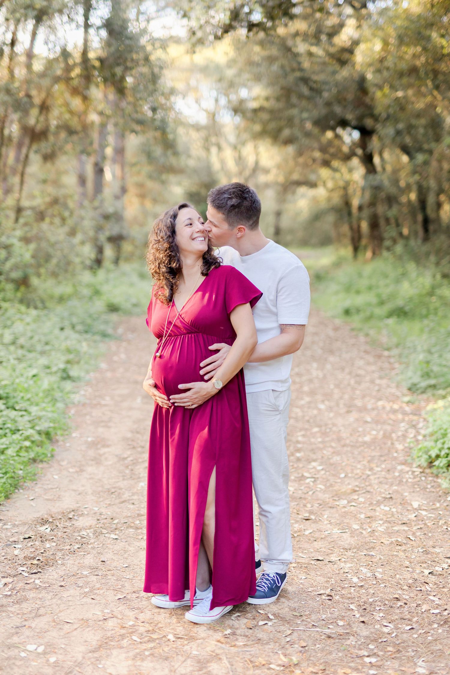 Romantic maternity photos captured on a nature trail with warm evening light filtering through trees.