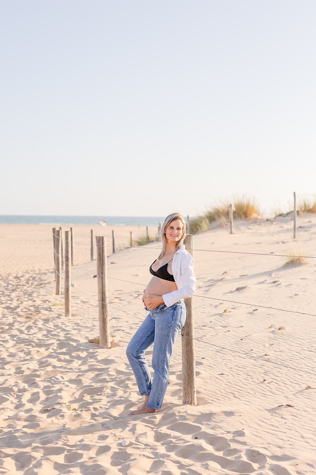 Woman in jeans posing against wooden posts on a sandy beach at sunset creates dynamic compositions.