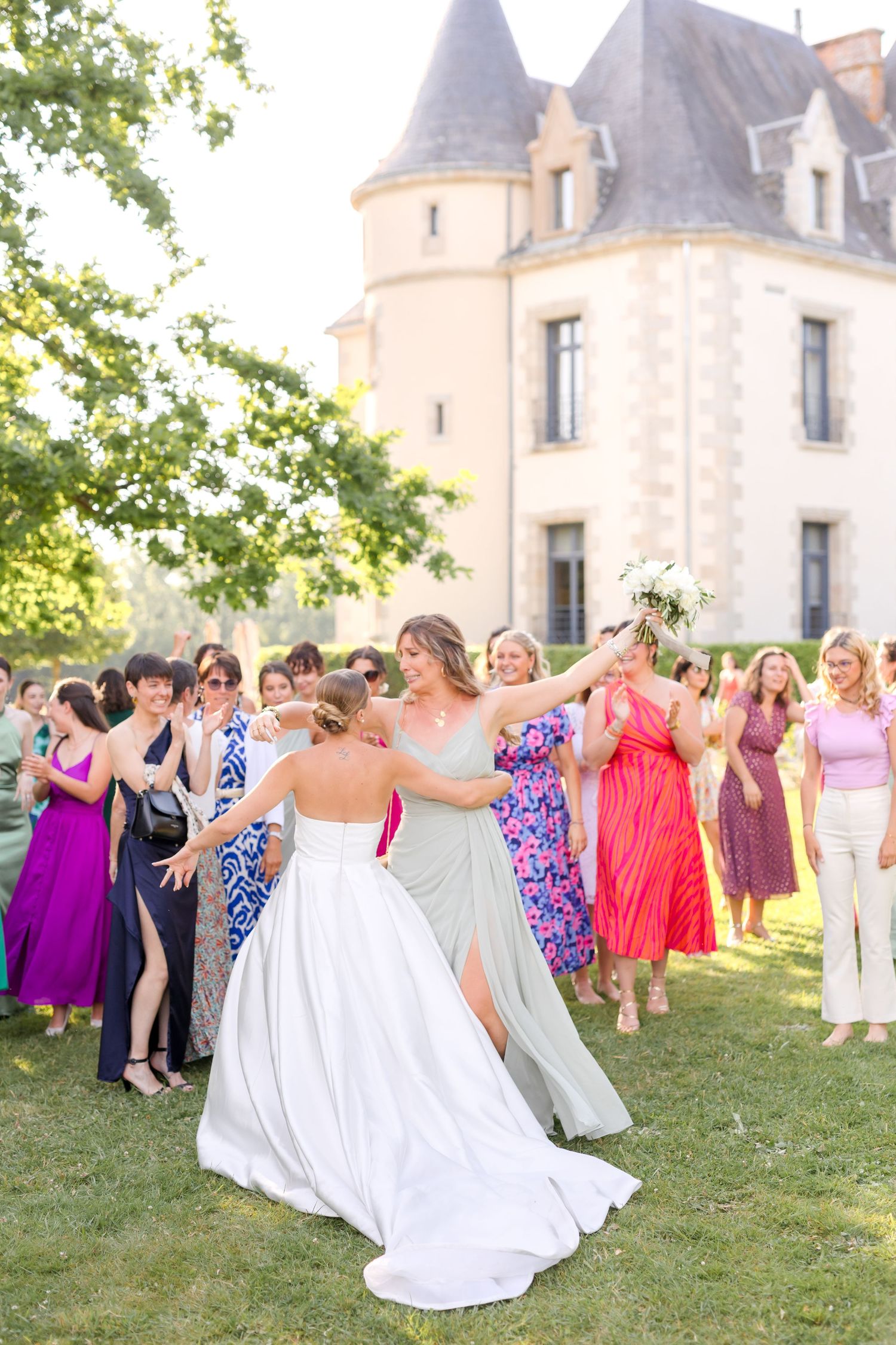 Wedding party dances and celebrates on lawn with beautiful castle architecture in background.