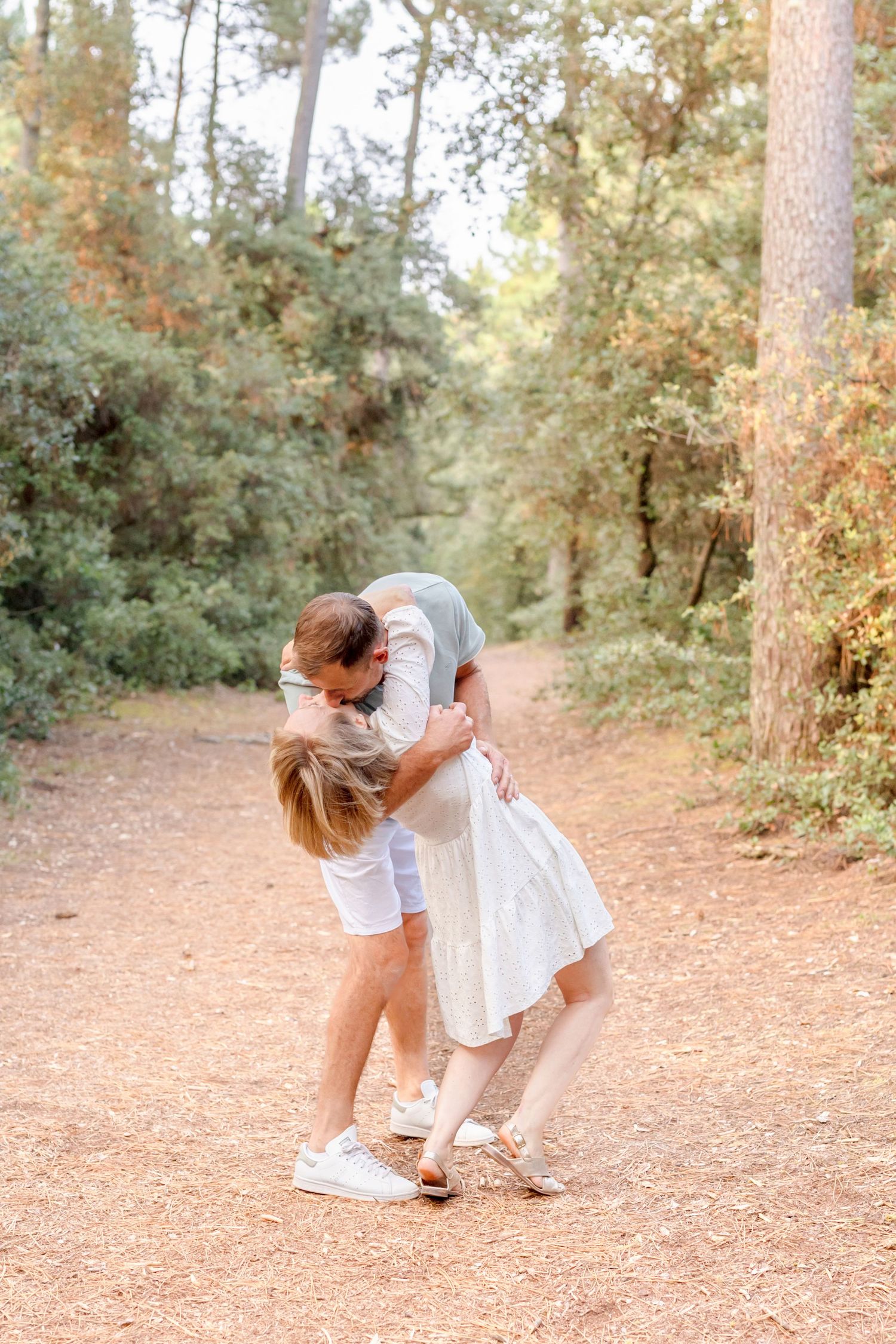 A romantic moment captured on a sunlit forest path as a couple shares a sweet embrace.