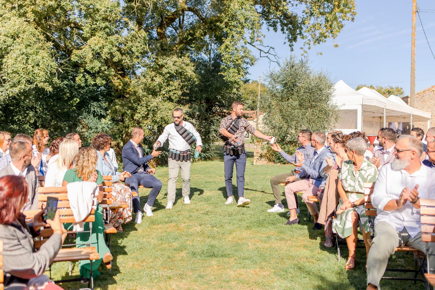 Musicians perform for seated wedding guests on a sunny lawn.
