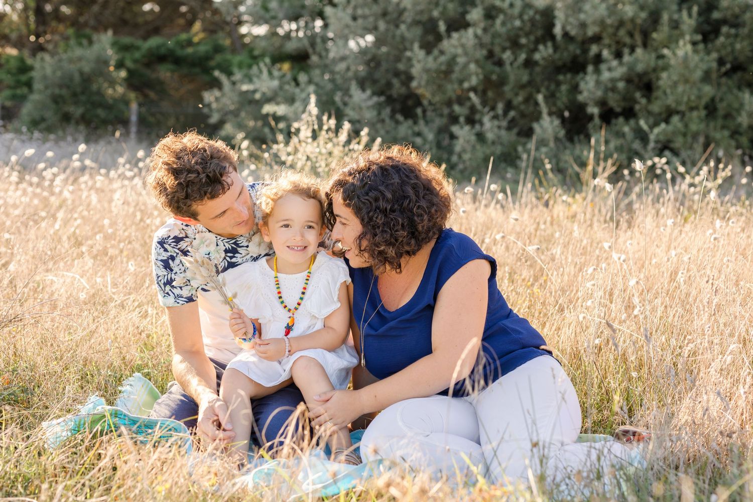 Intimate family moment shared while sitting in tall grass during golden hour.