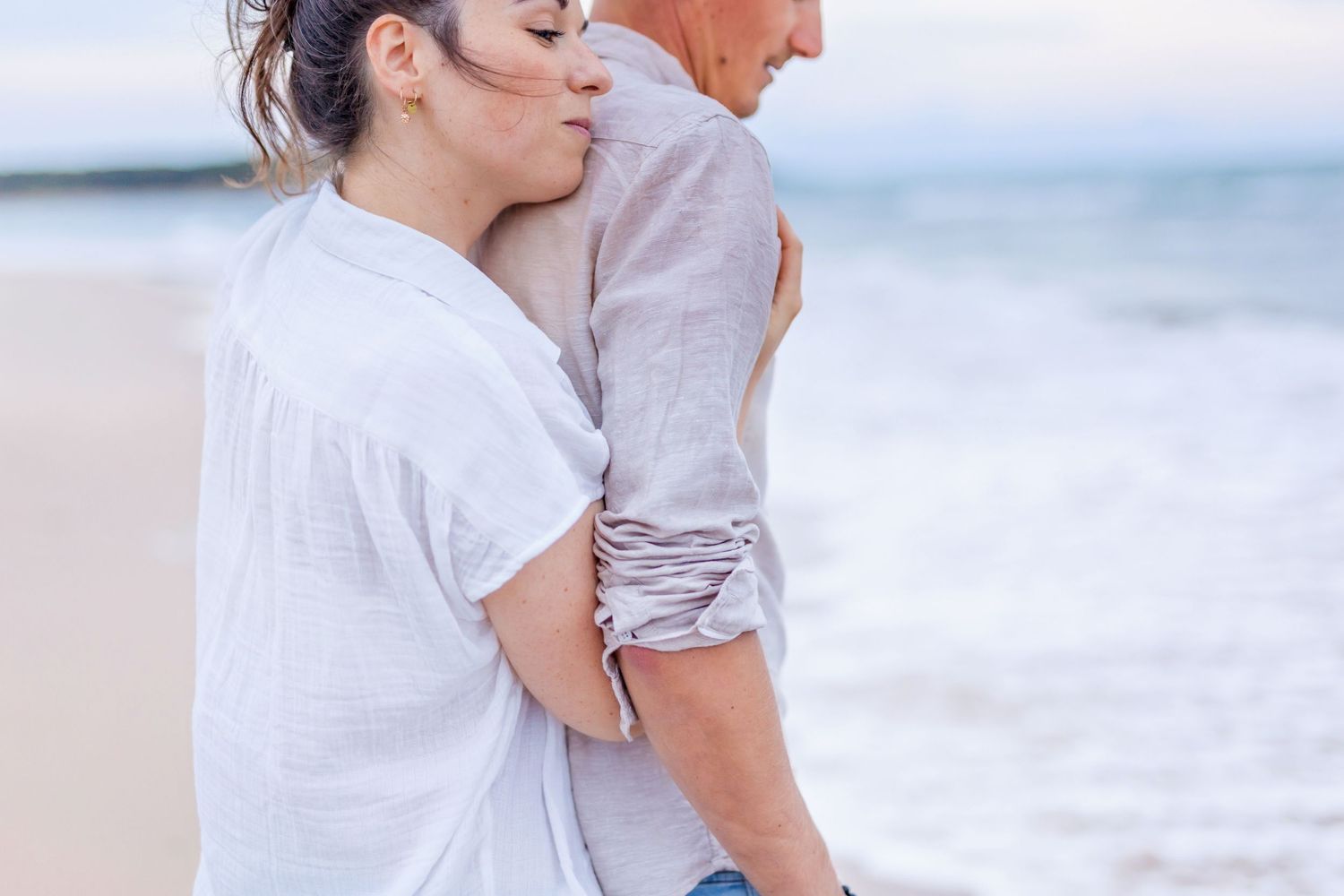 A tender moment captured between two people in casual attire on a beach.