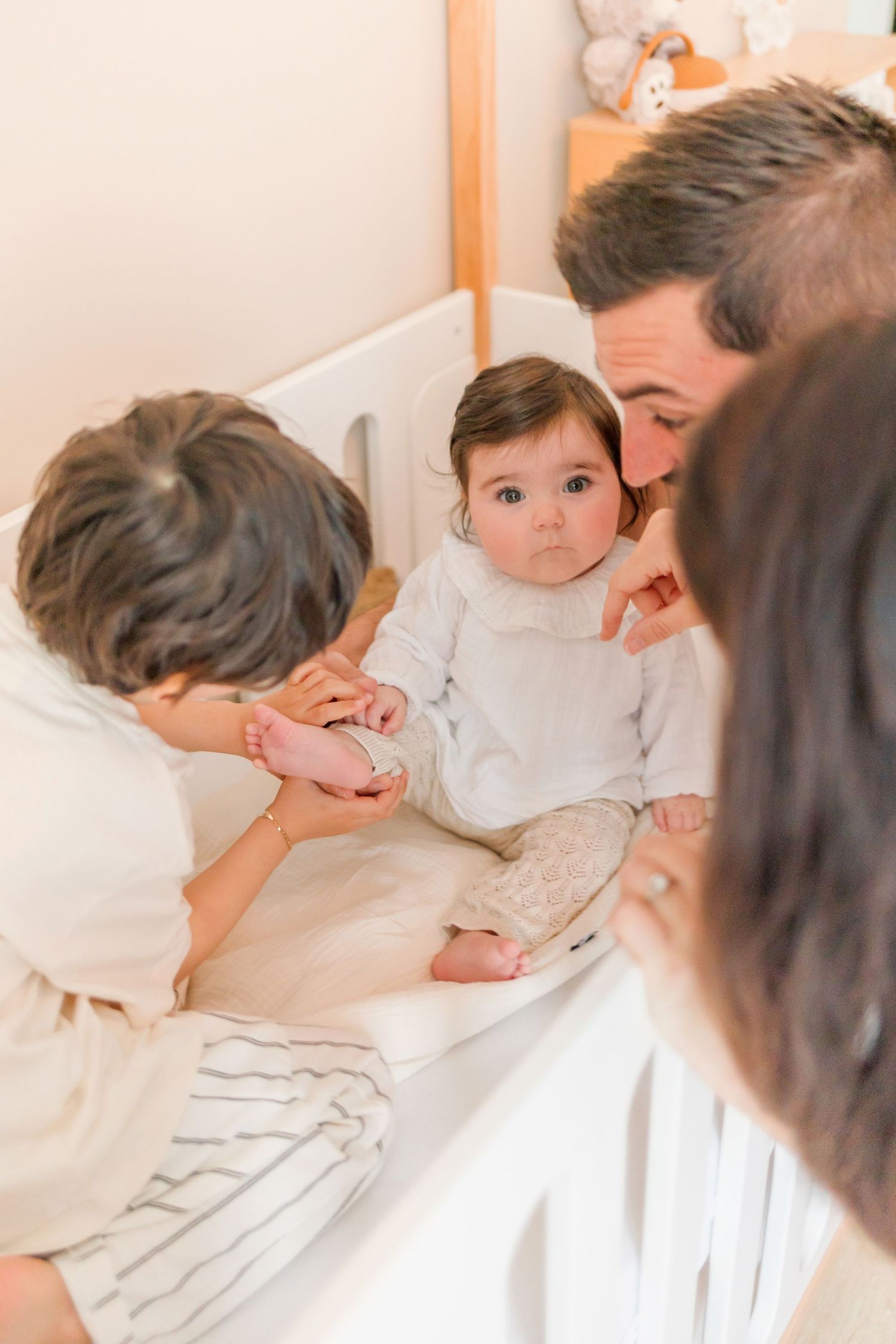 Intimate family moment captured in soft lighting around white crib.