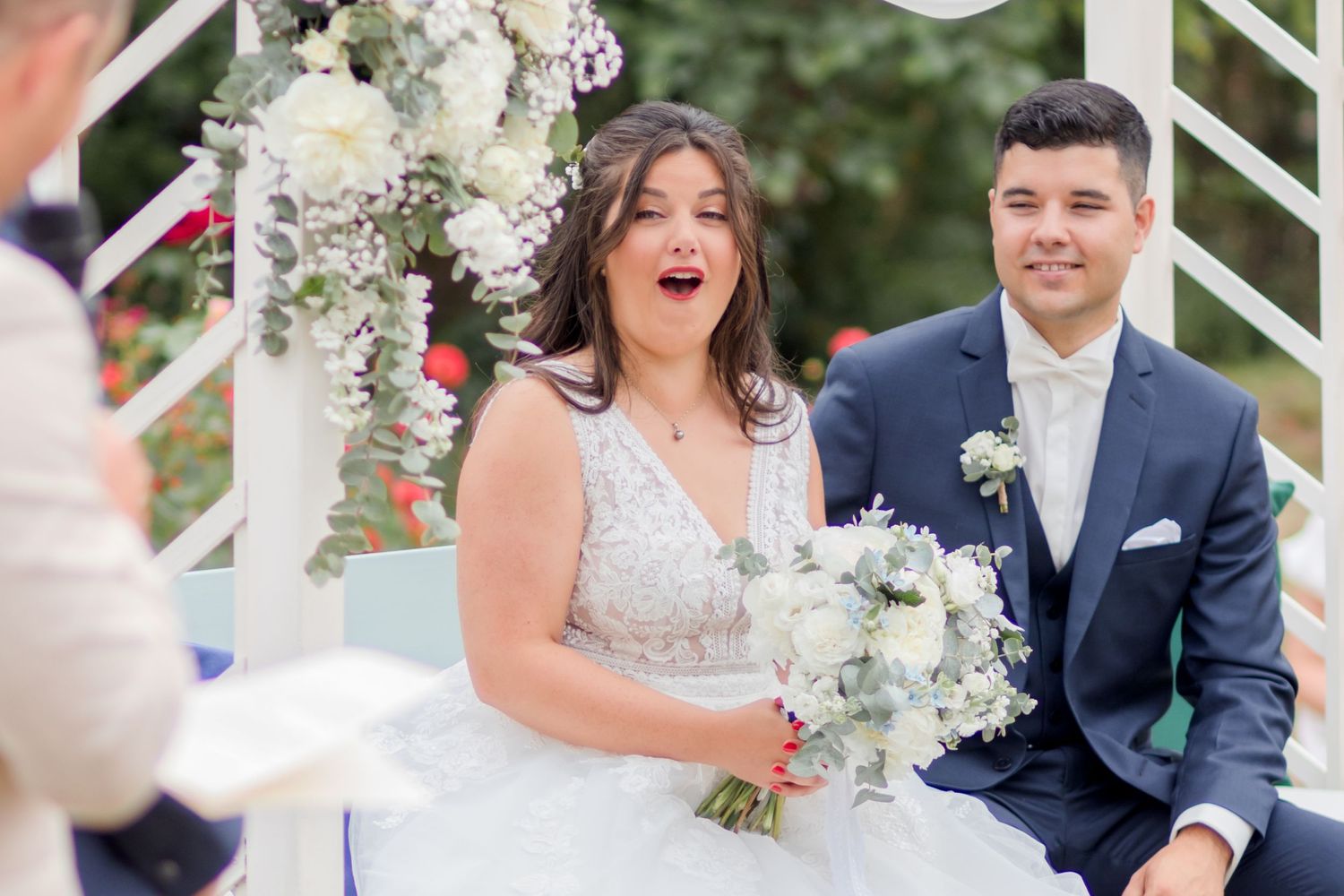 Couple sharing joyful moment during outdoor wedding ceremony under floral arch.