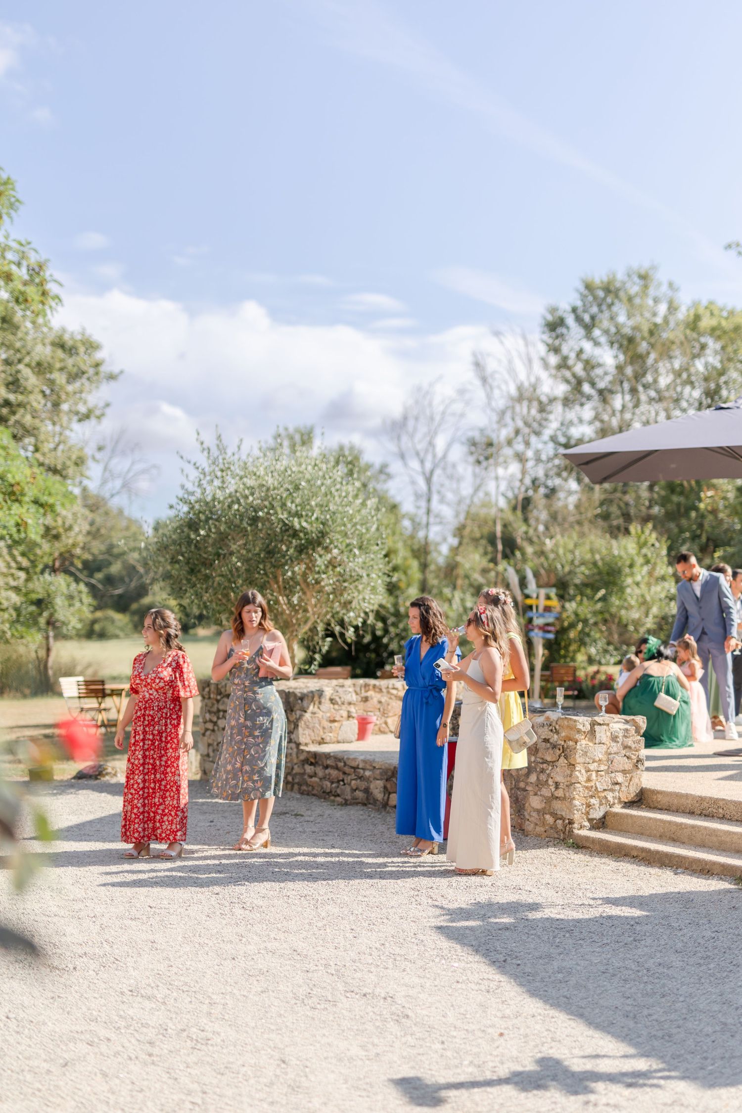 Outdoor garden party with guests mingling on a stone patio under blue skies.