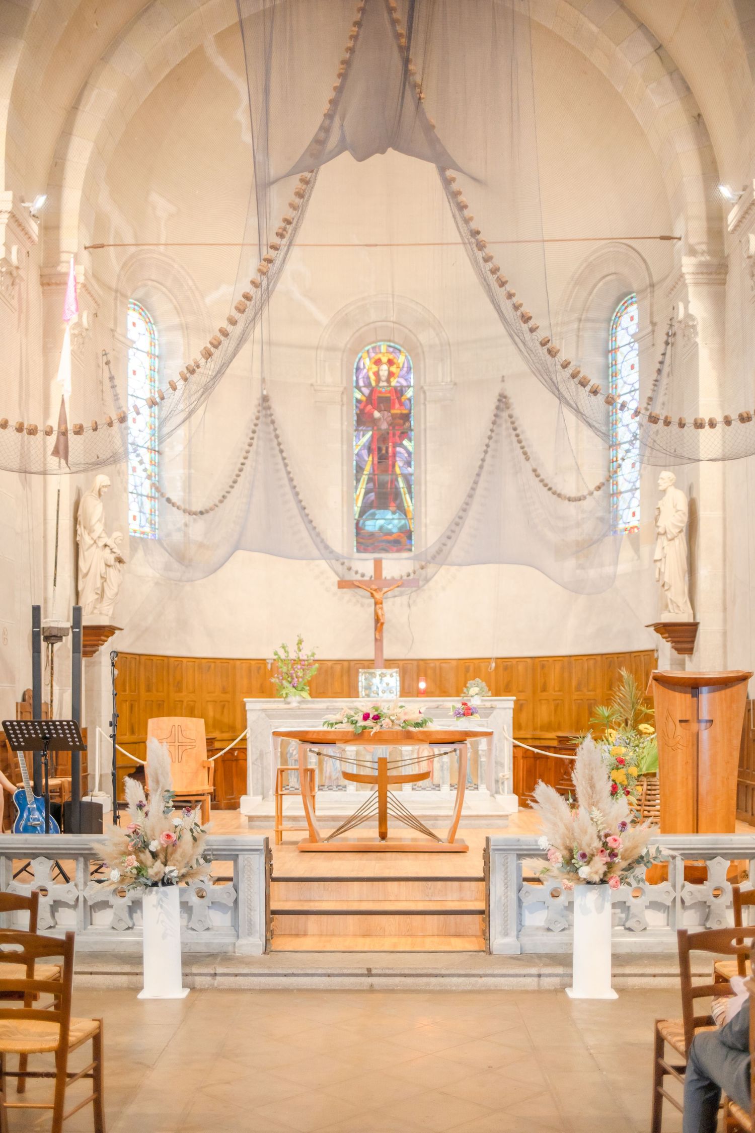 Interior of a church sanctuary decorated with white drapes and floral arrangements for a wedding ceremony.