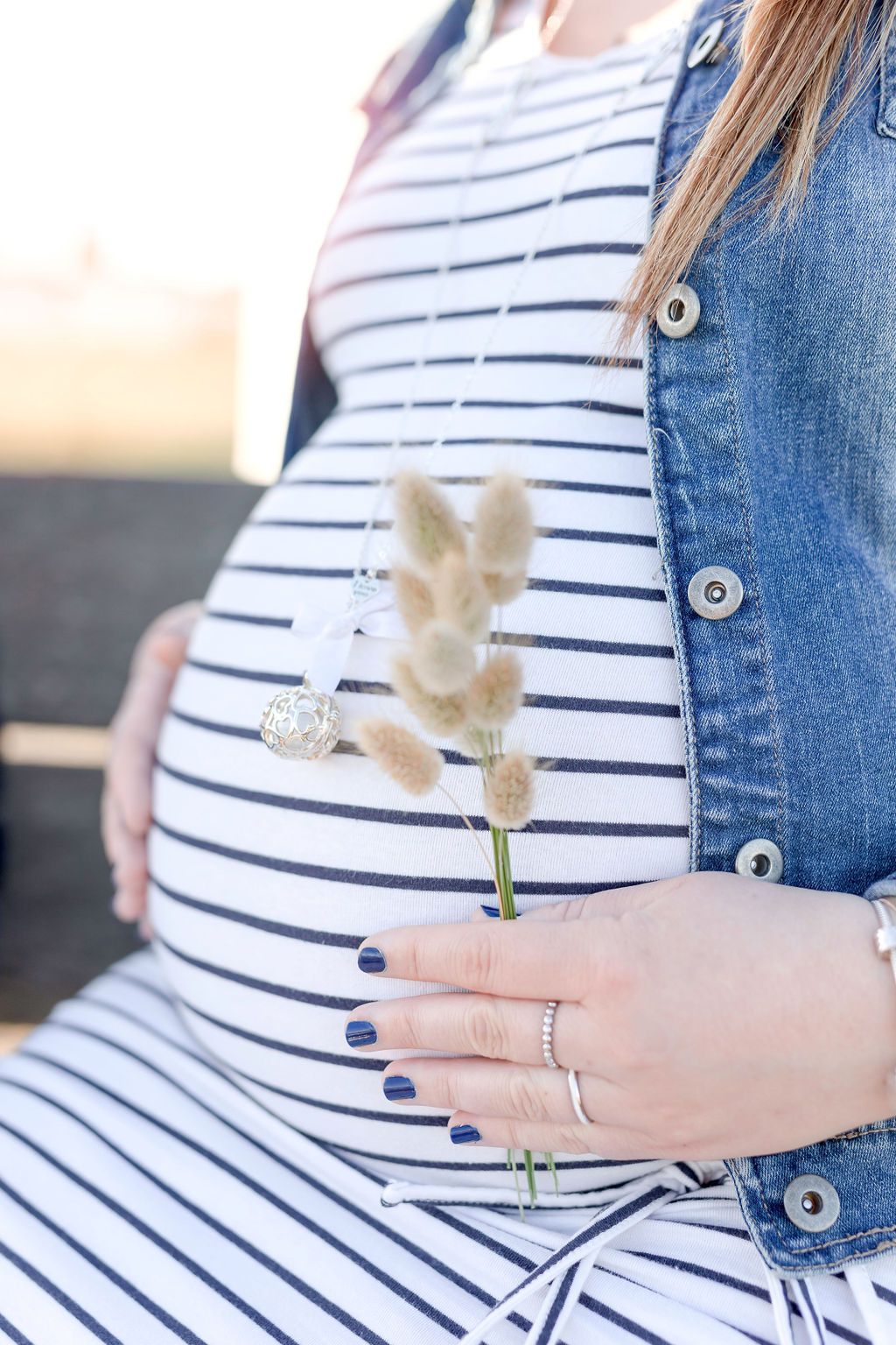 Close-up of dried flower against striped maternity dress with denim jacket.