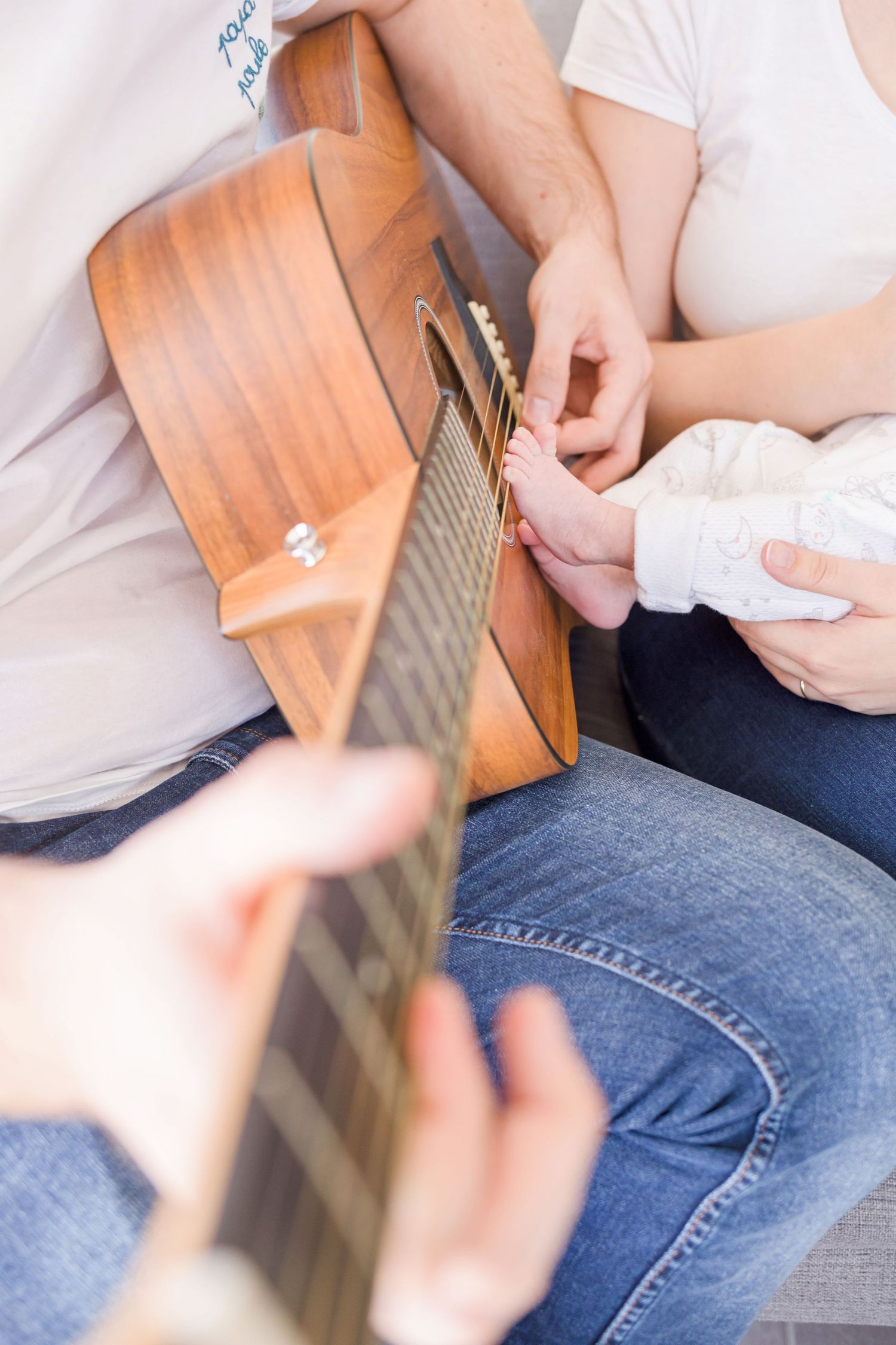 Close-up shot of hands strumming a wooden ukulele while seated on a couch in jeans.