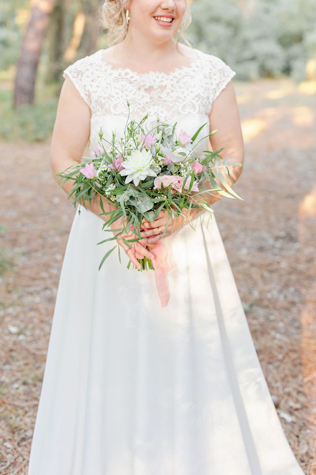 Close-up of a delicate bridal bouquet with pink flowers and greenery against a white wedding dress.