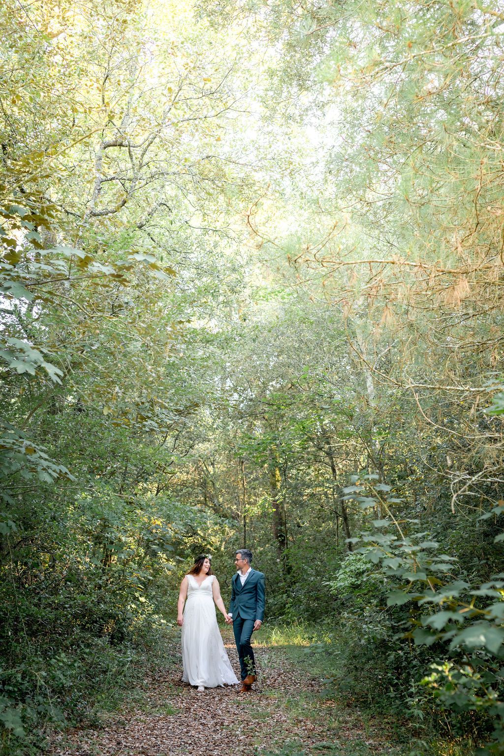Newlyweds share an intimate moment on a leaf-covered path through green forest.