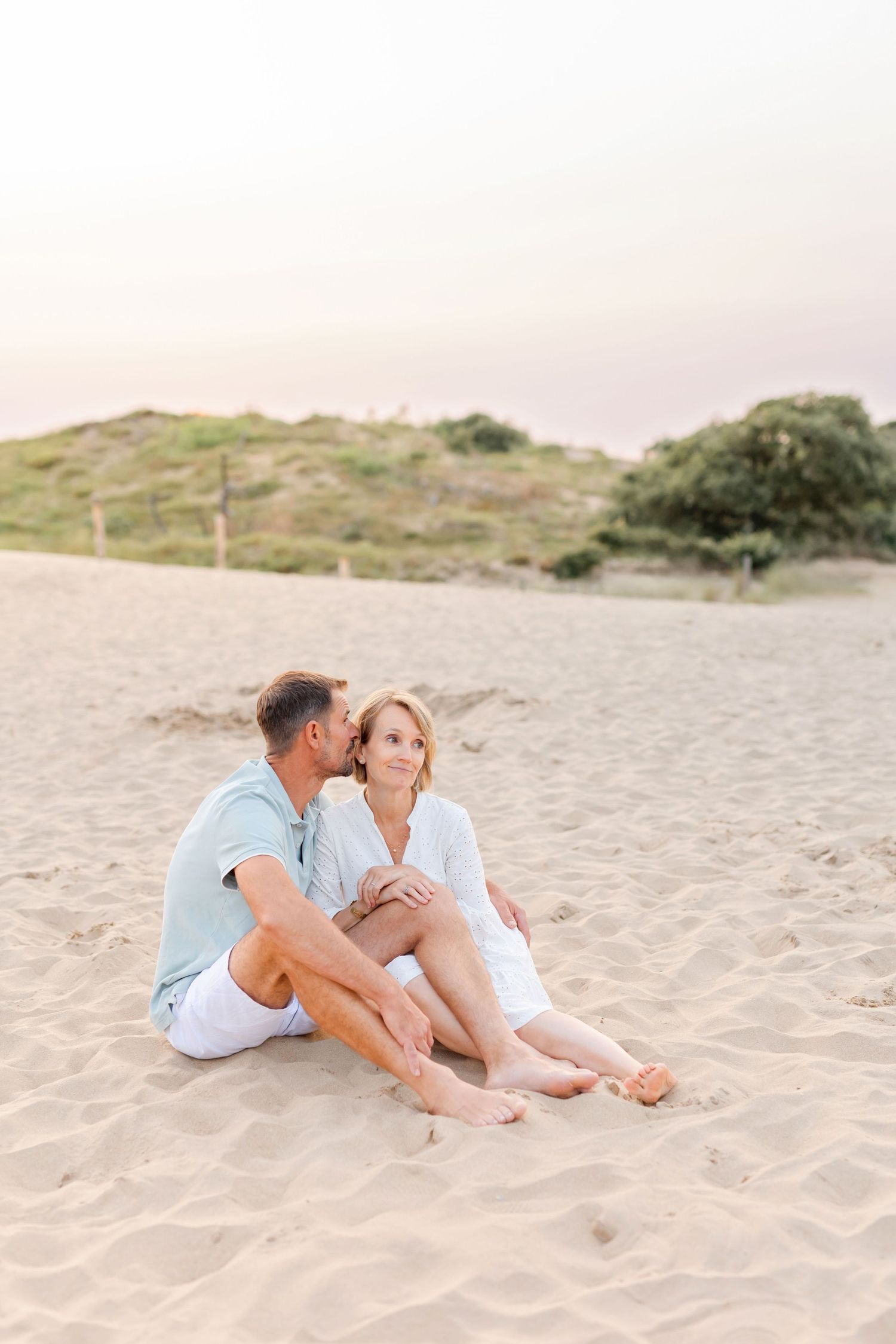 Couple sitting close together on sandy beach at sunset.