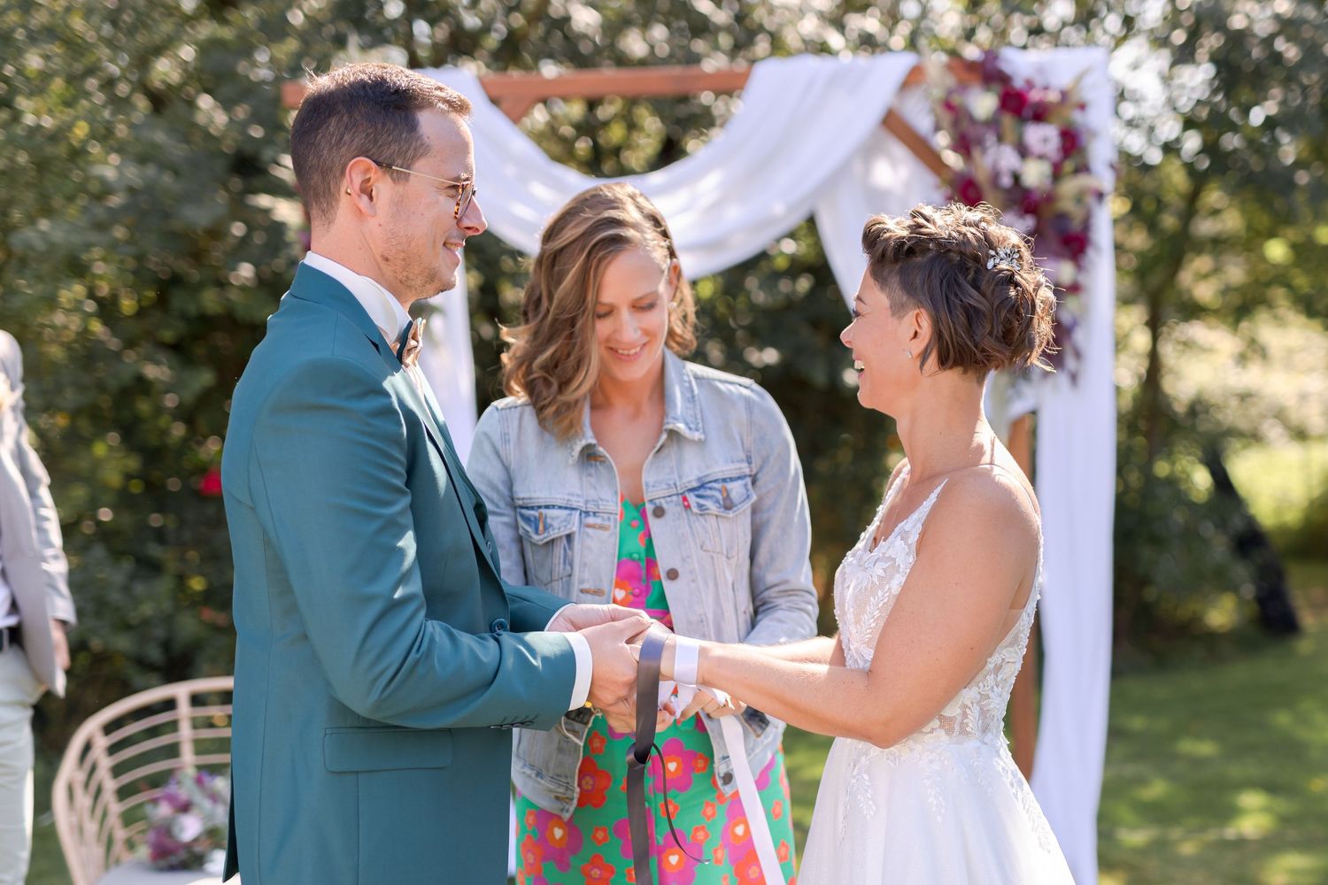 Intimate outdoor wedding ceremony under floral arch with couple exchanging vows.
