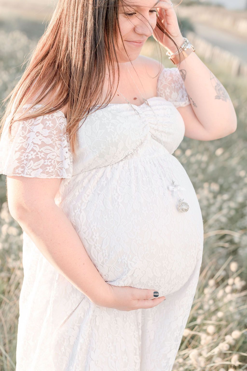 Soft focus maternity portrait highlighting lace sleeves and rounded belly.