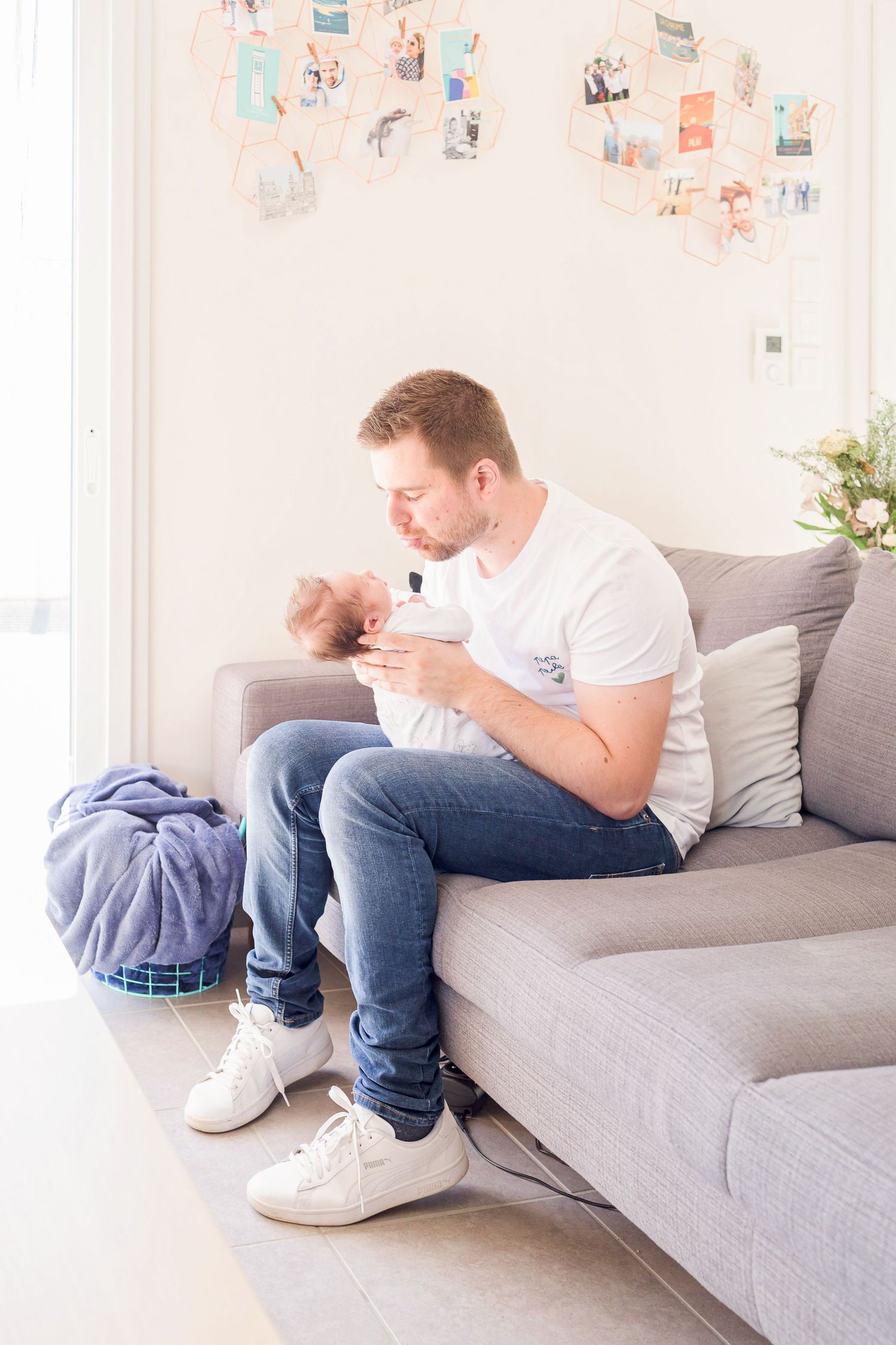 Person in white t-shirt and jeans sitting on gray couch looking down at something.