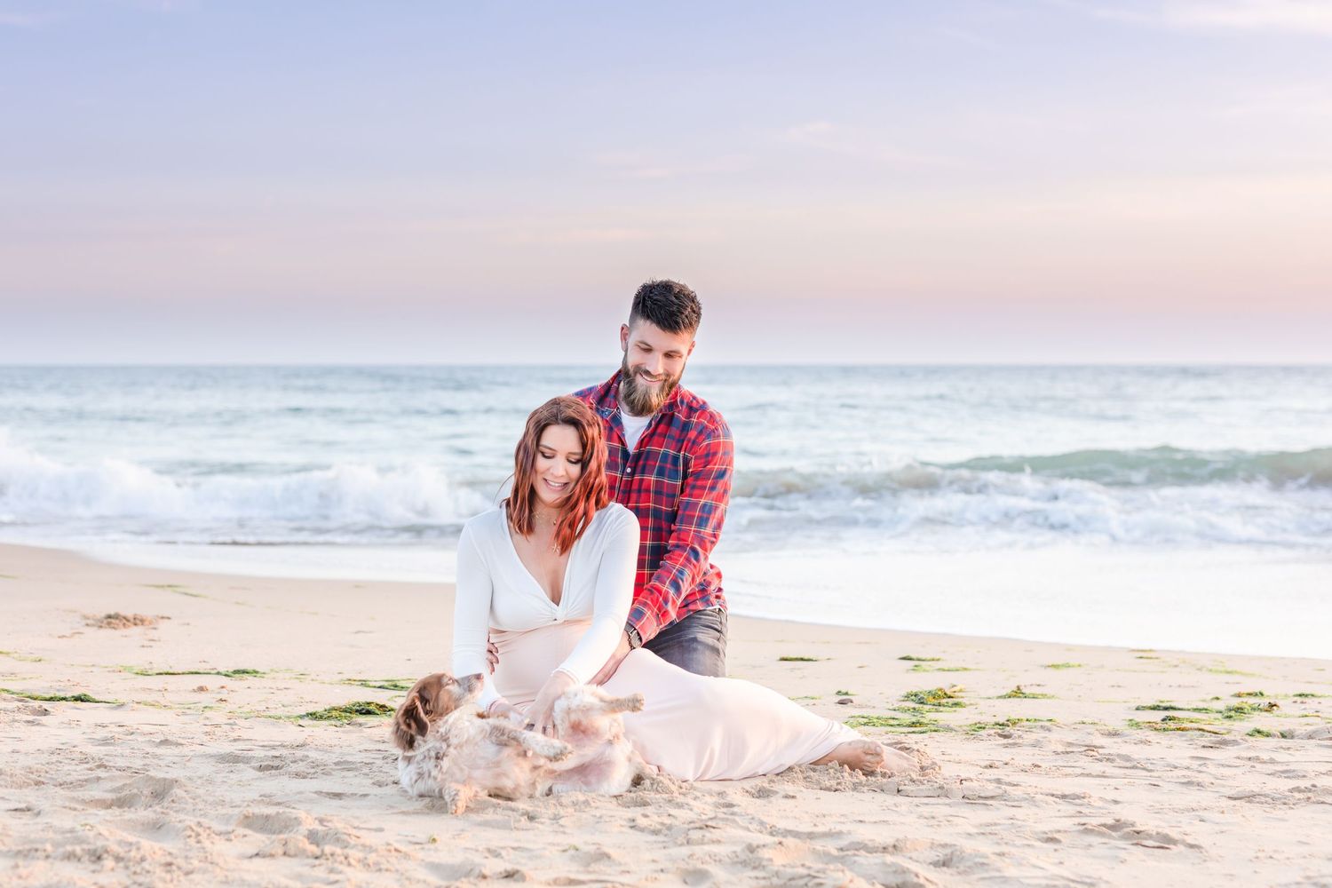 Romantic beach portrait of couple sitting in sand during golden hour.