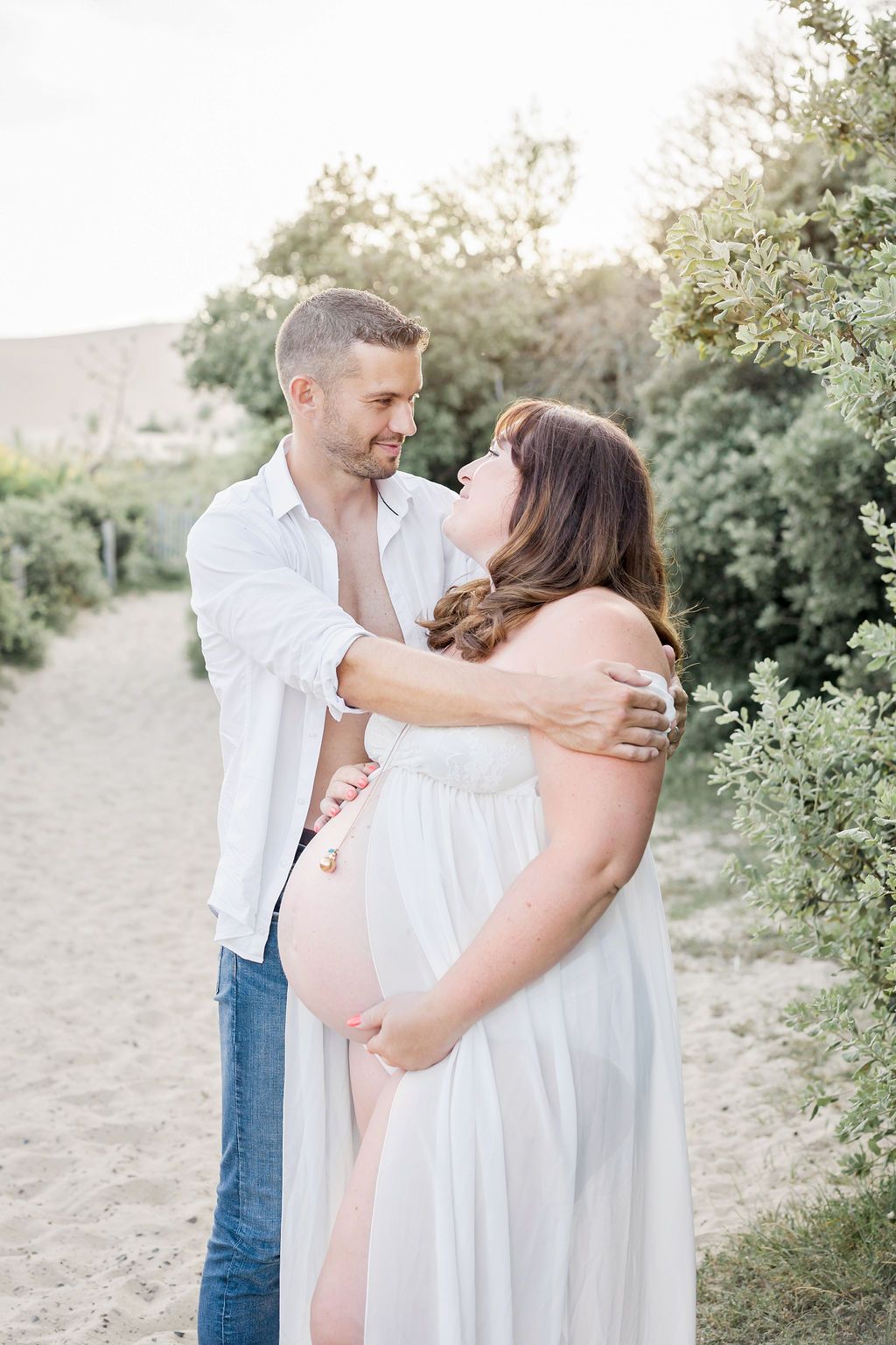An intimate maternity photo featuring a couple sharing a tender moment on a nature path at dusk.