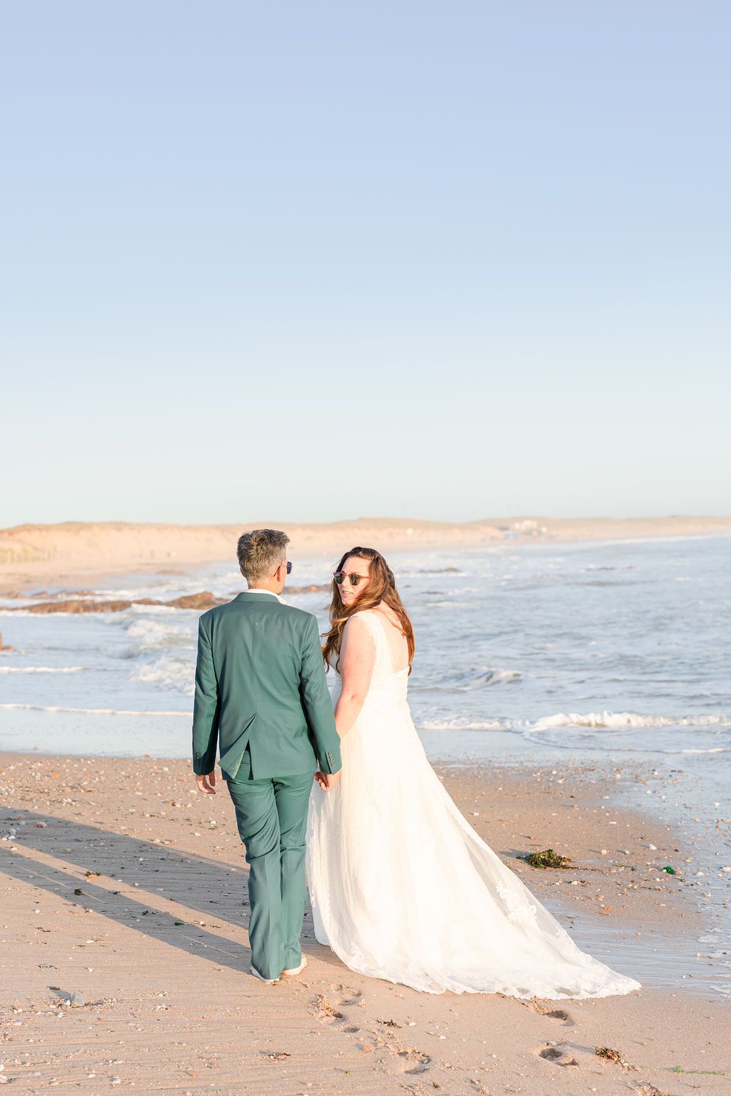 Romantic beach wedding couple walking along shoreline at sunset.