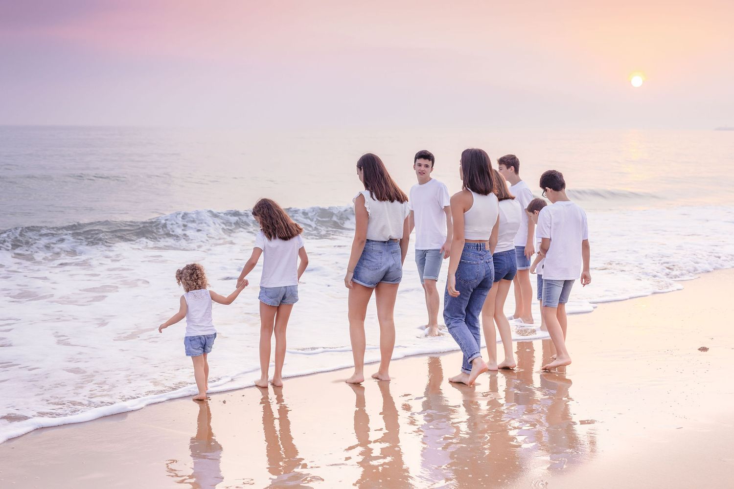 Extended family enjoys sunset beach time together wearing matching casual attire.