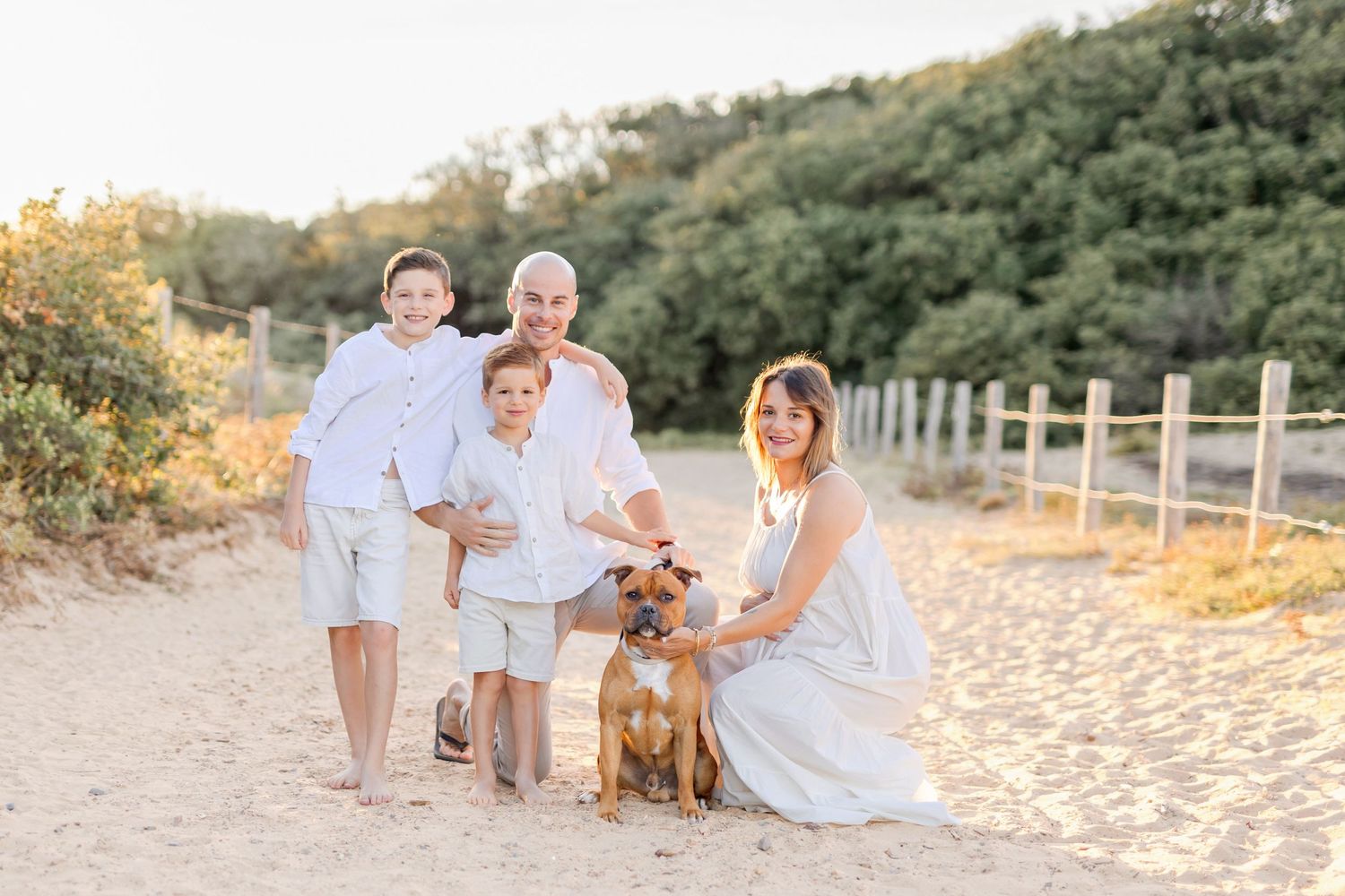 Family and dog pose together on sandy beach during golden hour photoshoot.
