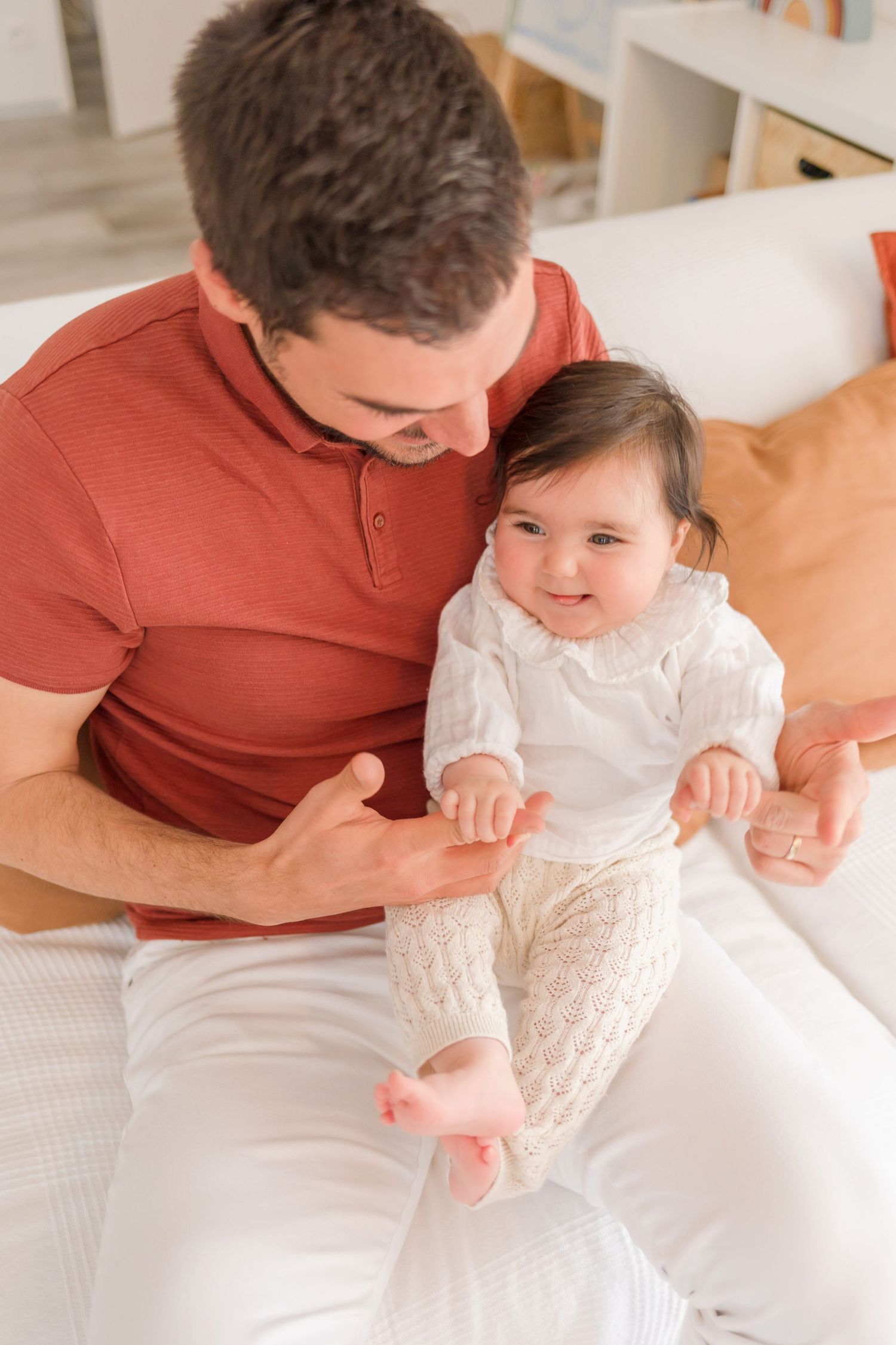 Tender family interactions on white bedding with someone wearing a red shirt playing with a baby.