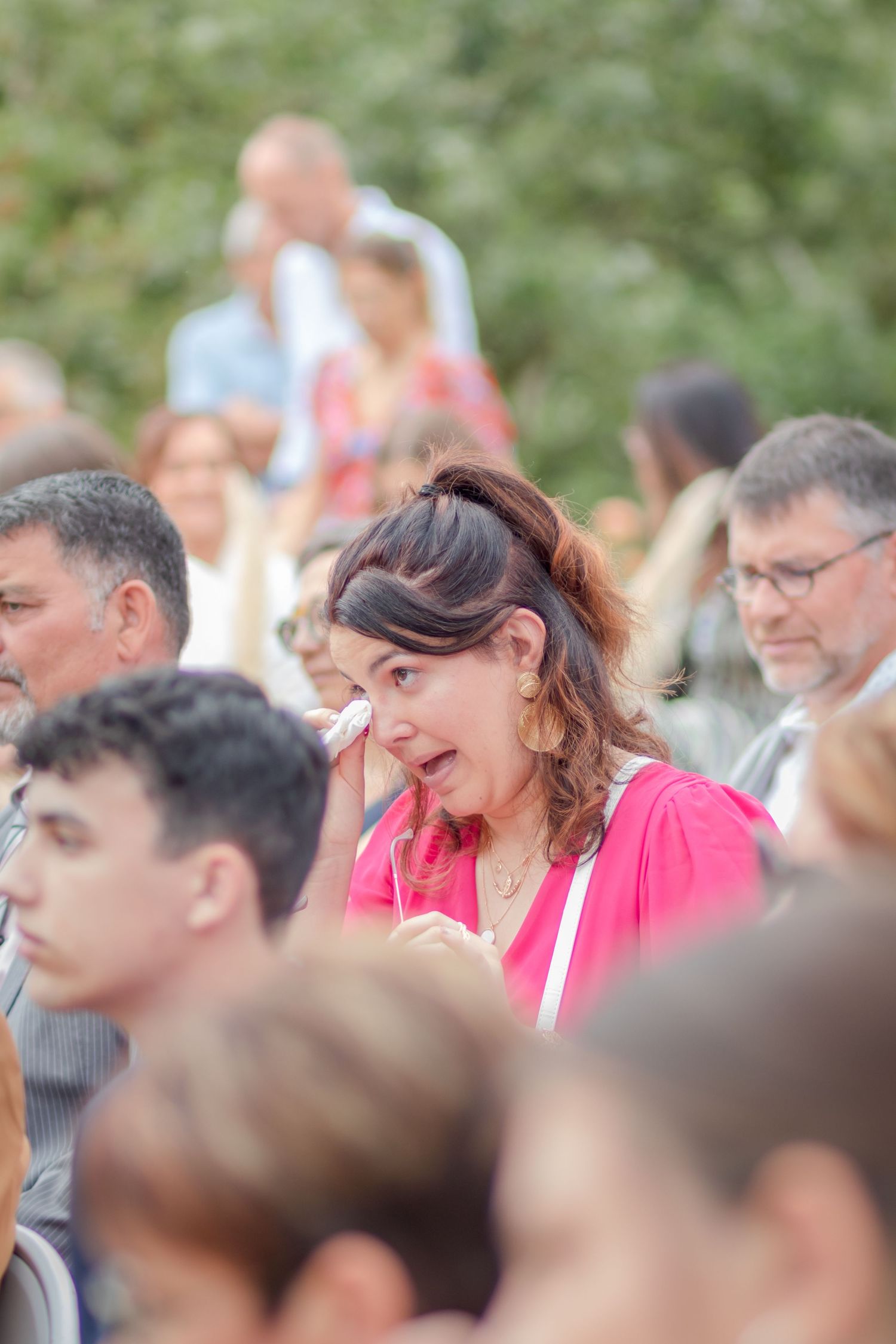 Guest in pink dress wipes away tears during emotional outdoor wedding moment.