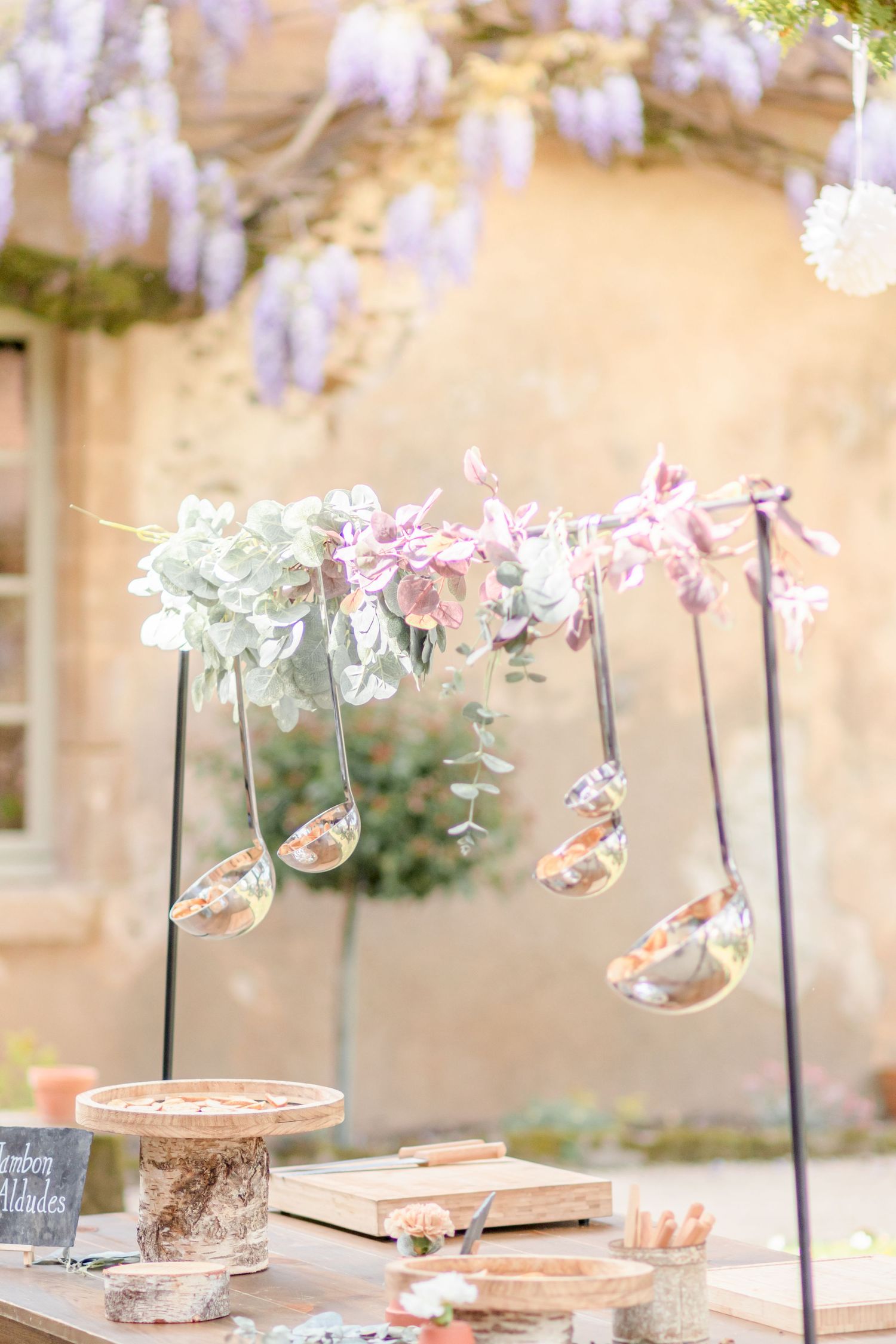 Decorative hanging glass vessels with floral arrangements under purple wisteria blooms.