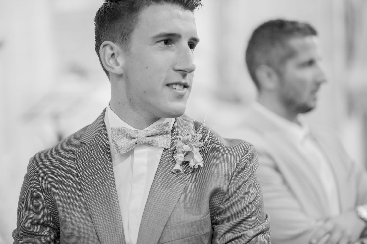 Close-up portrait of a groom wearing a gray suit and bow tie with boutonniere.