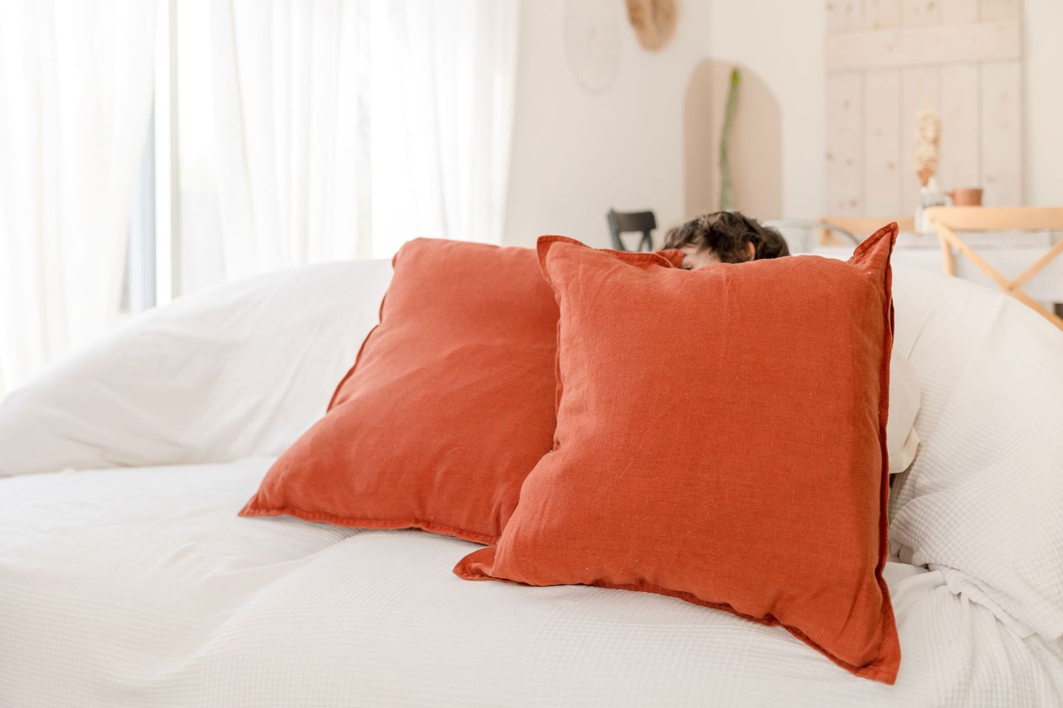 Two coral orange pillows on a white bed with natural lighting from a window.