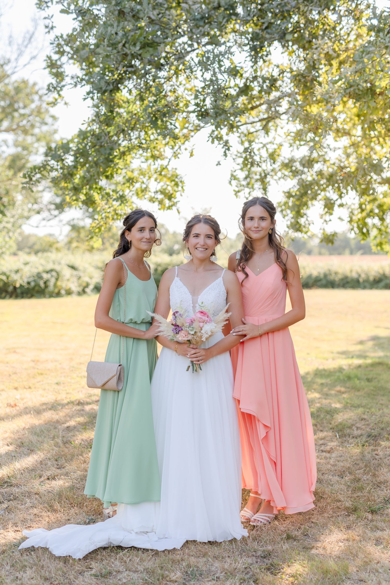 Bridesmaids in mint green and coral dresses pose together in a sunlit outdoor setting.