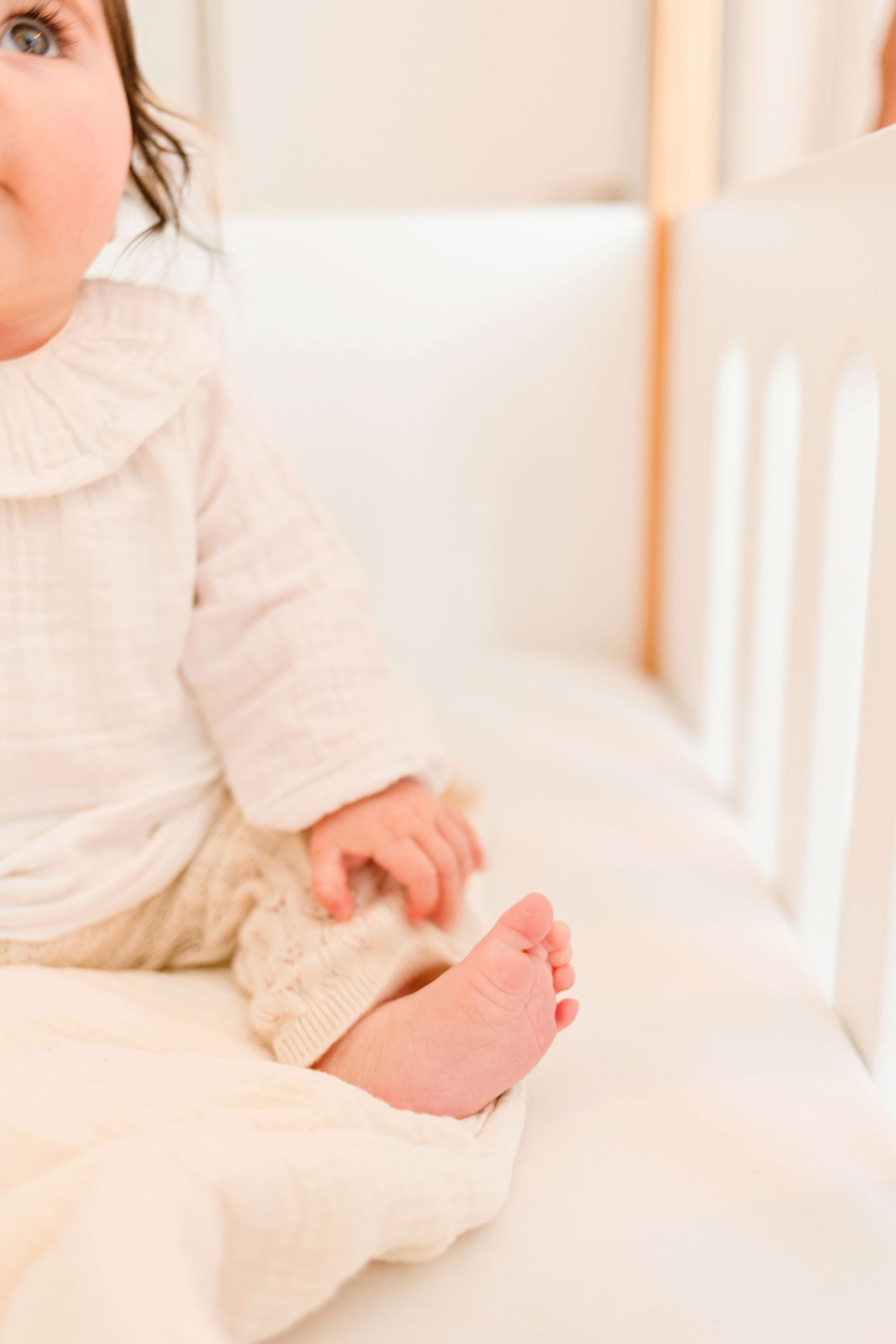 Baby's feet peek out from white clothing in bright nursery setting.