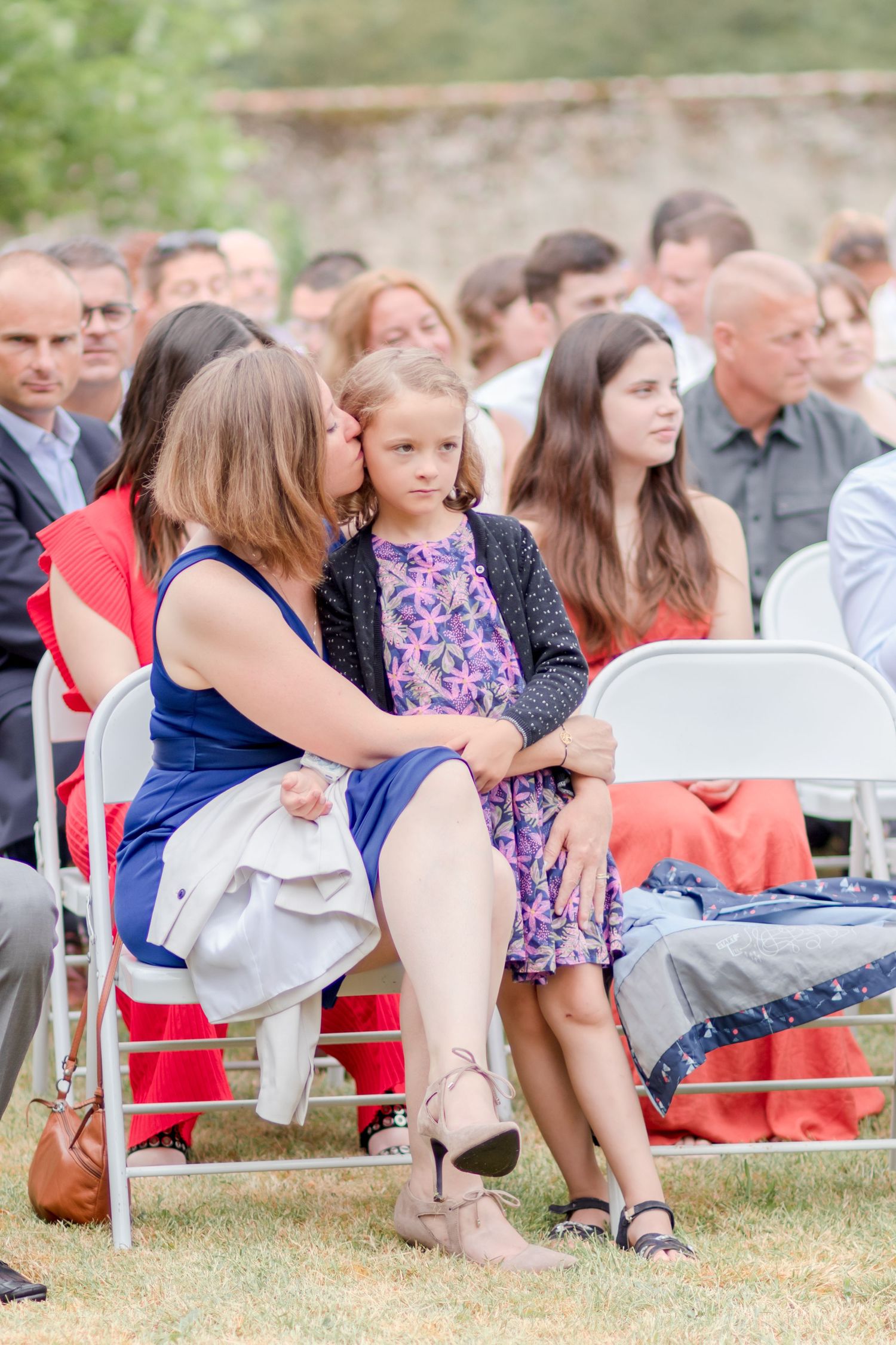 Guests seated in folding chairs at an outdoor wedding ceremony in a garden setting.