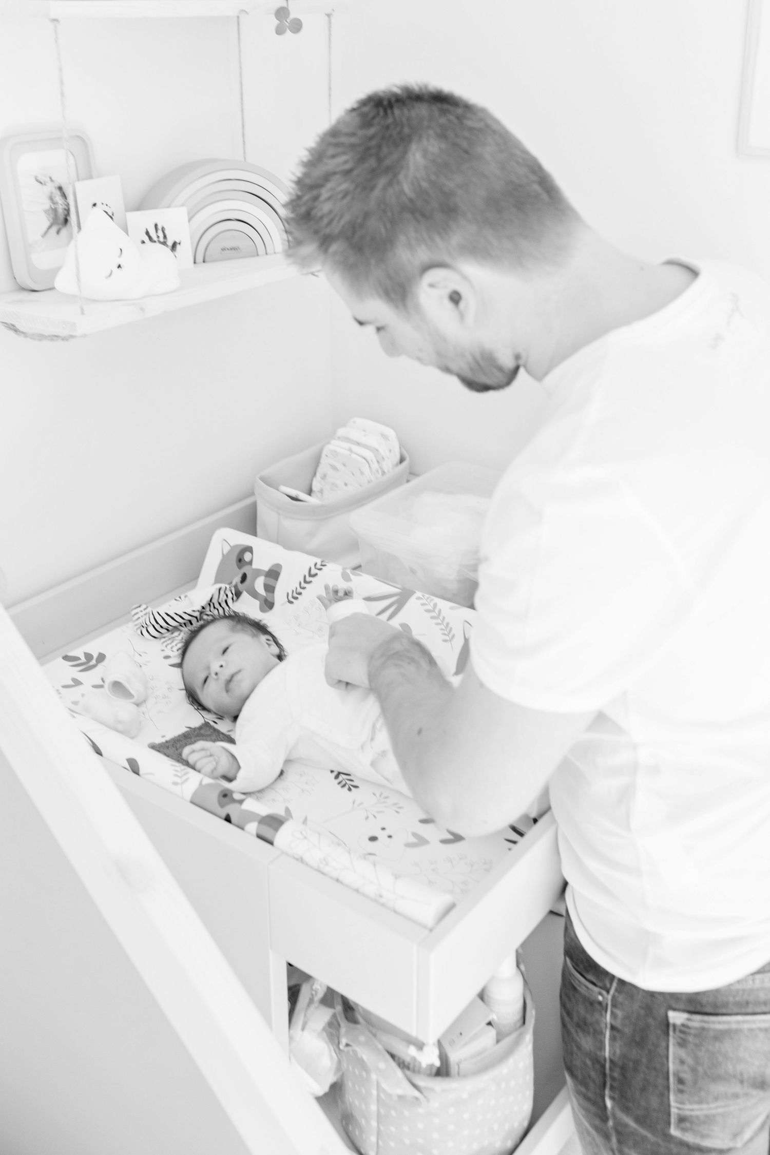 Changing table scene in a bright nursery with rainbow decor on shelf.
