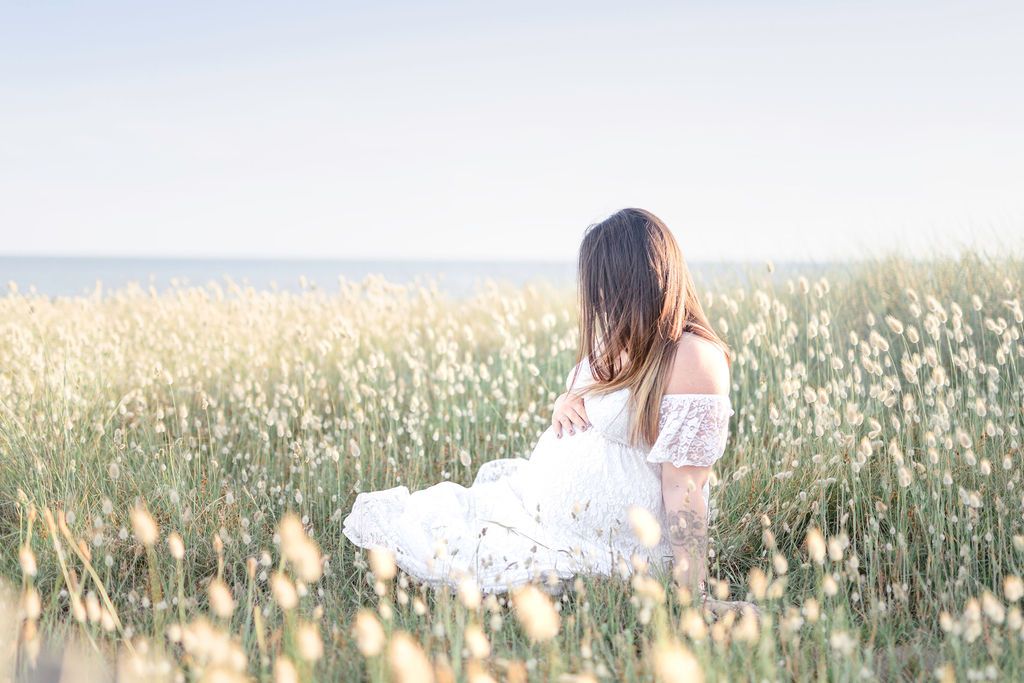 Person in white dress sitting among wildflowers by the ocean.