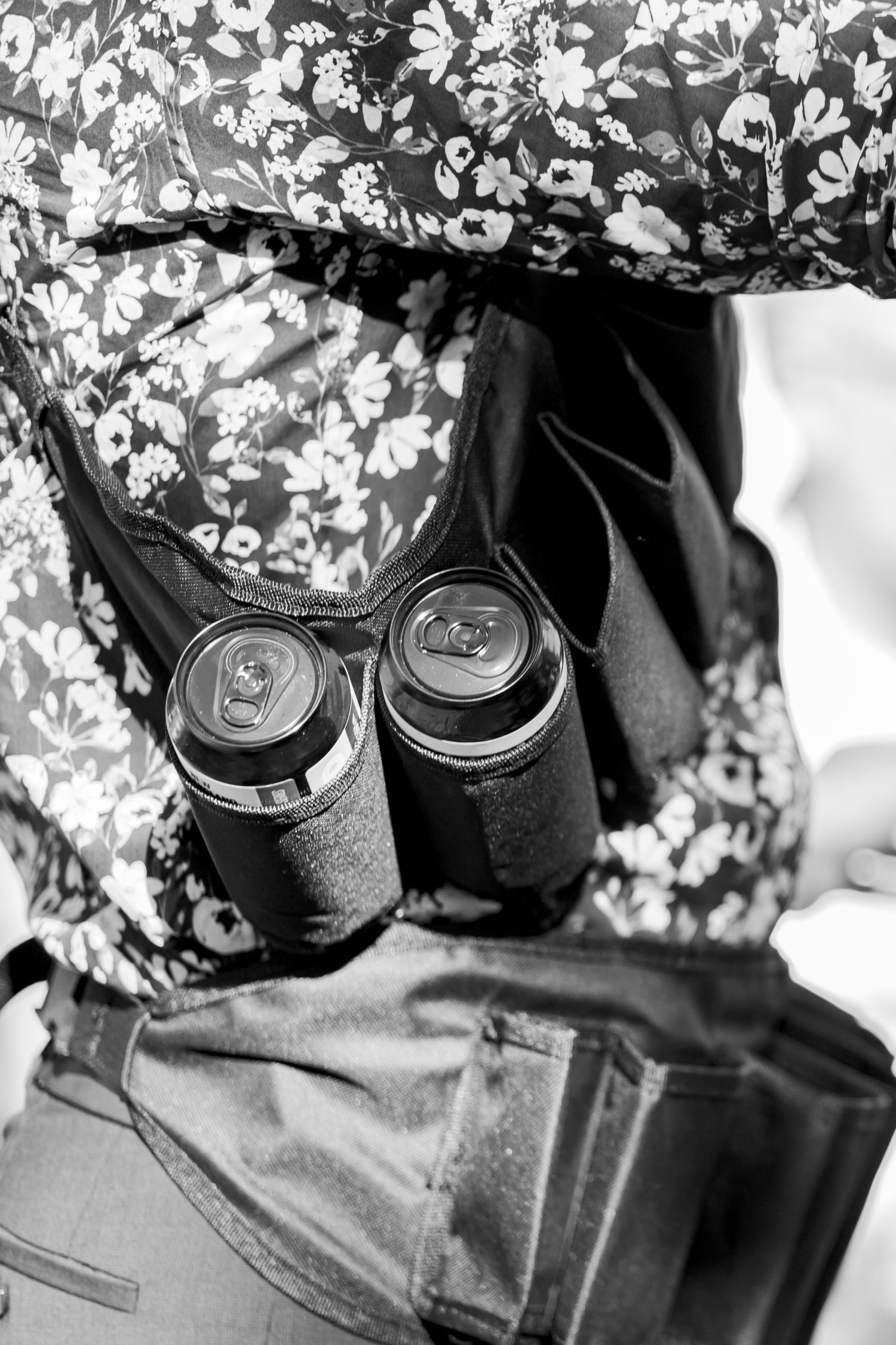 Black and white photo of two drink cans in a floral patterned bag.