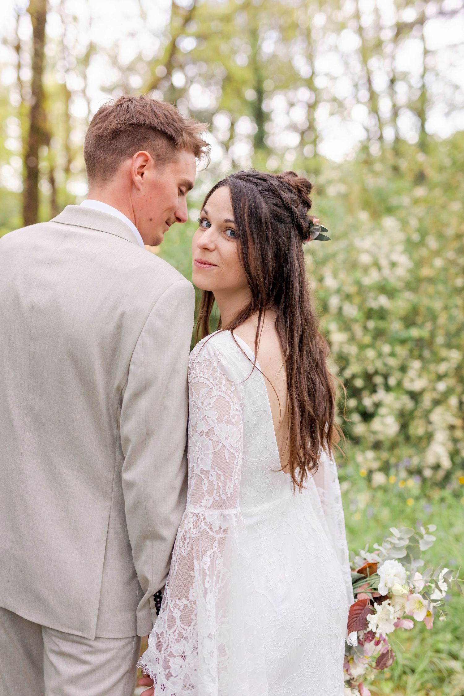 A romantic moment between newlyweds in a sunlit forest setting.