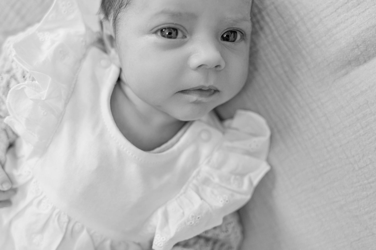 A black and white portrait of a baby wearing a white ruffled dress.