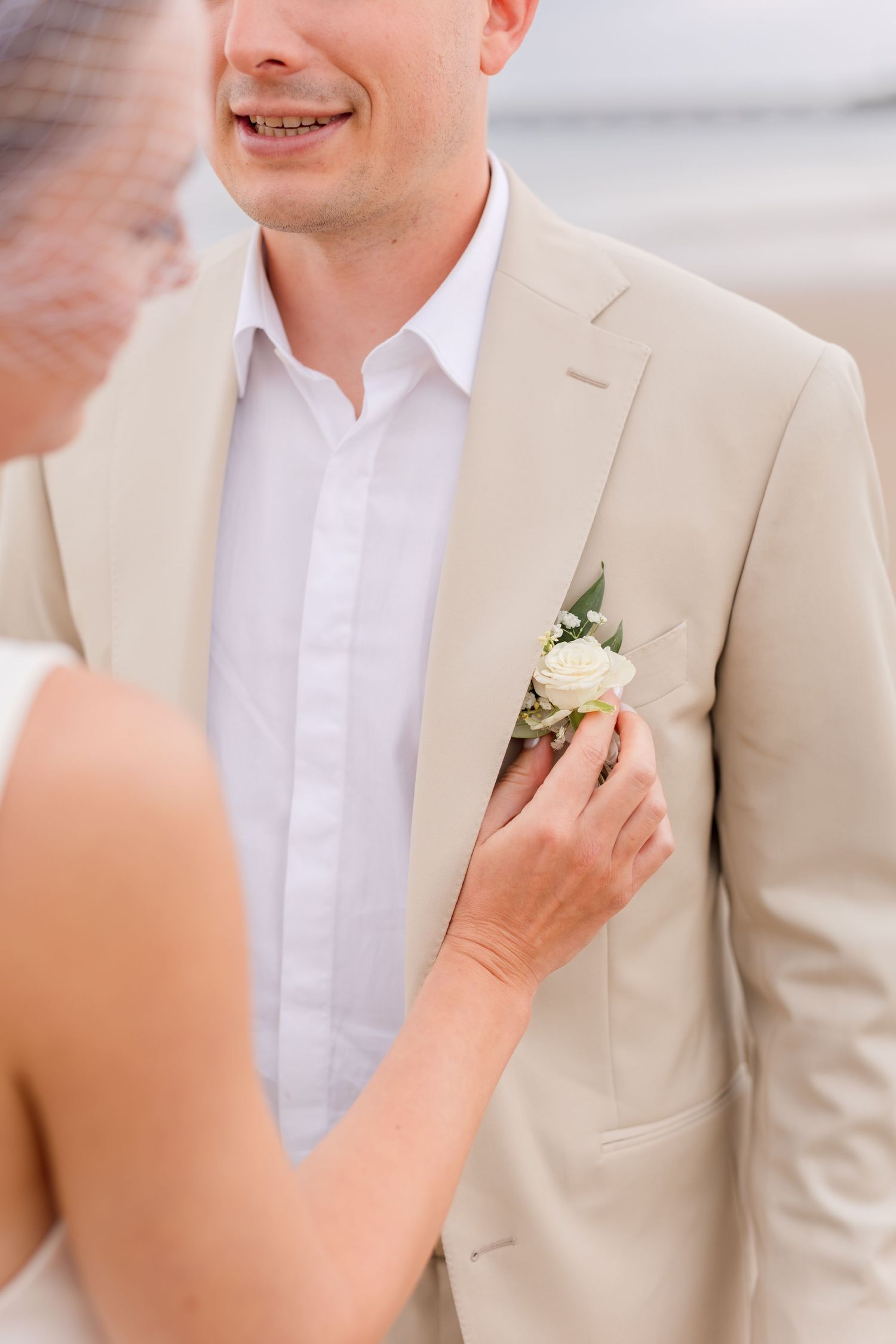 Someone pins a white rose boutonniere on a groom's beige suit lapel.