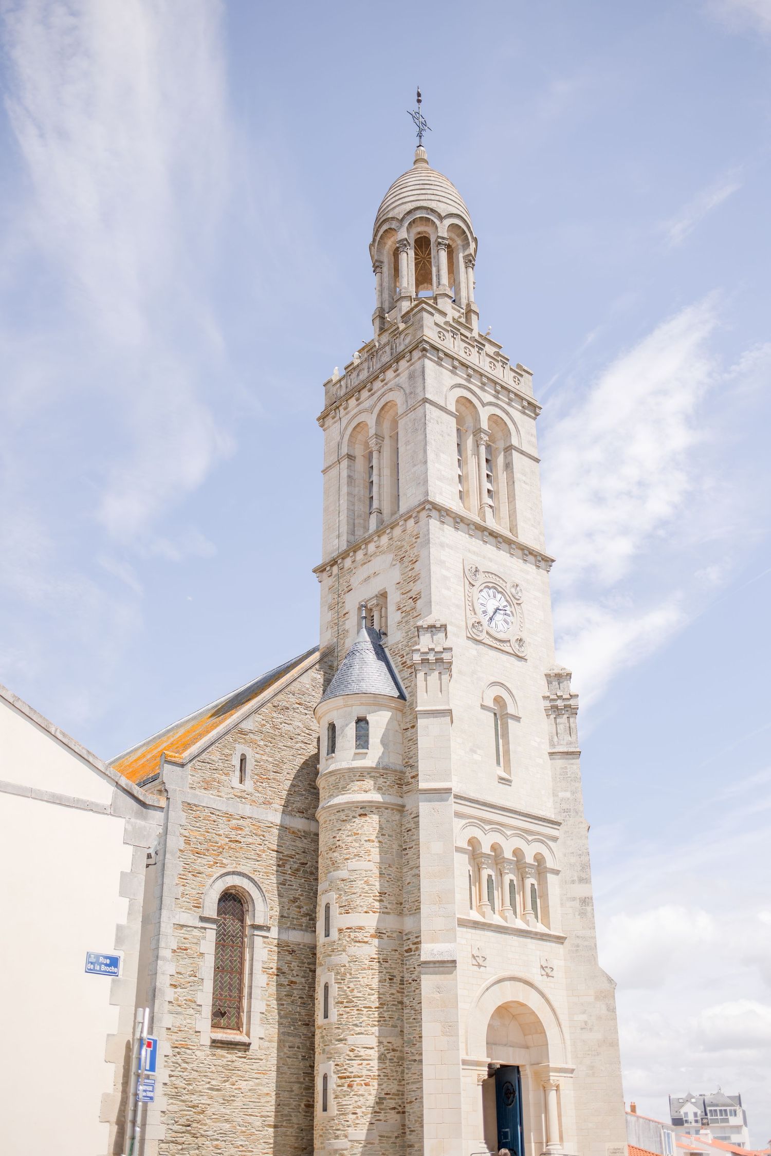 Beautiful white stone church with gothic architecture and bell tower against a bright blue sky.