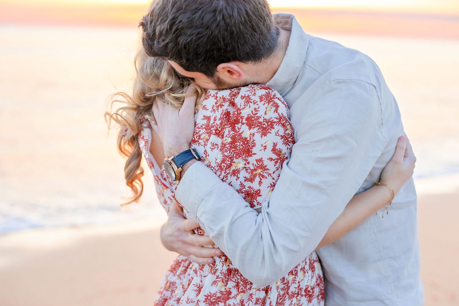 Romantic couple embracing on beach during sunset photoshoot.
