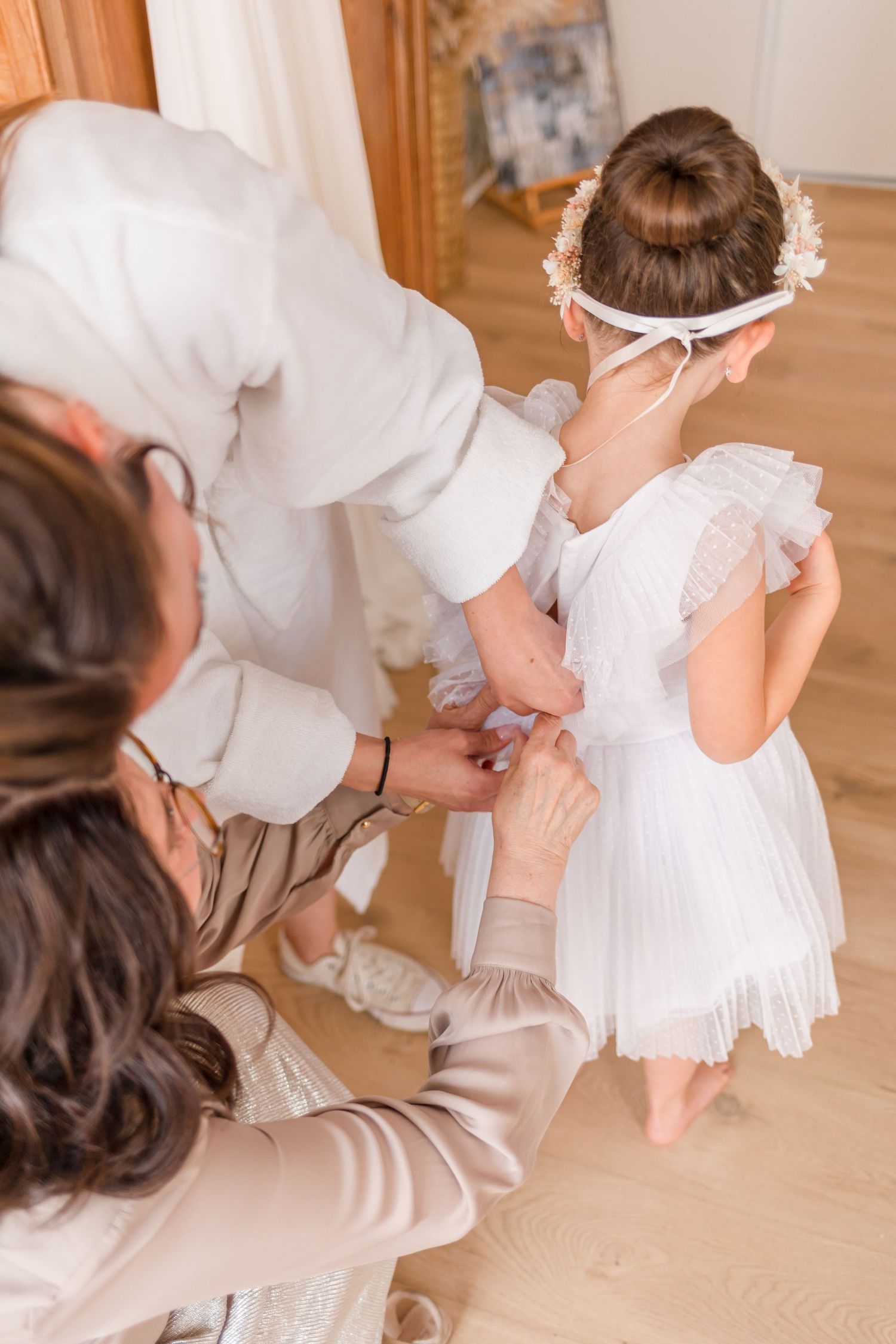 A behind-the-scenes moment of someone helping a small child in a white dress with final adjustments.