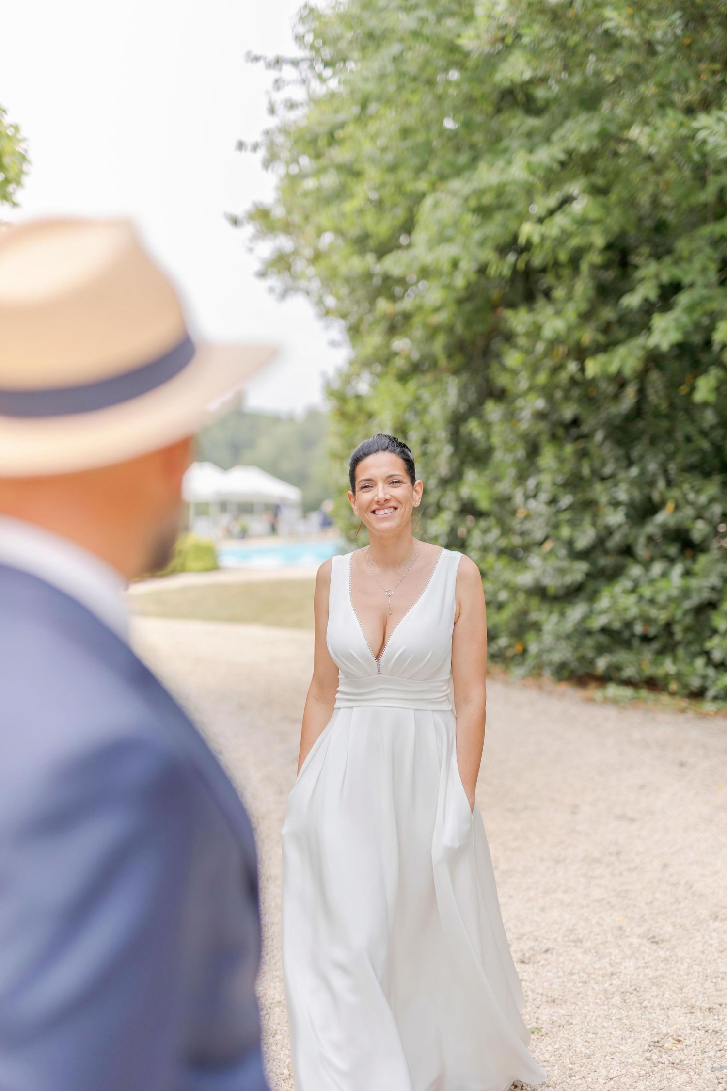 A bride in a flowing white gown stands on a gravel path near a historic building.
