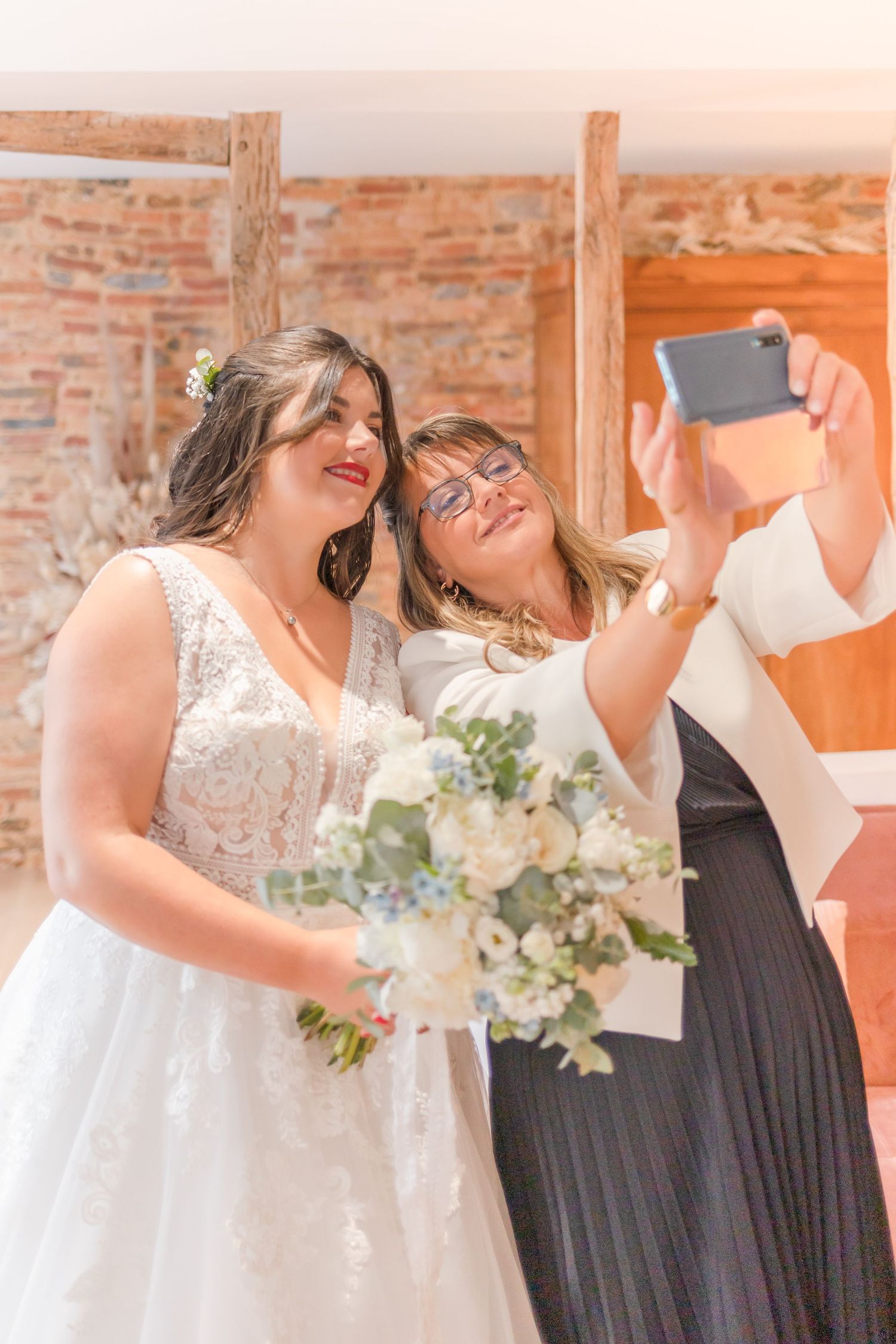A candid selfie moment captured during wedding preparations in a rustic brick-walled room.