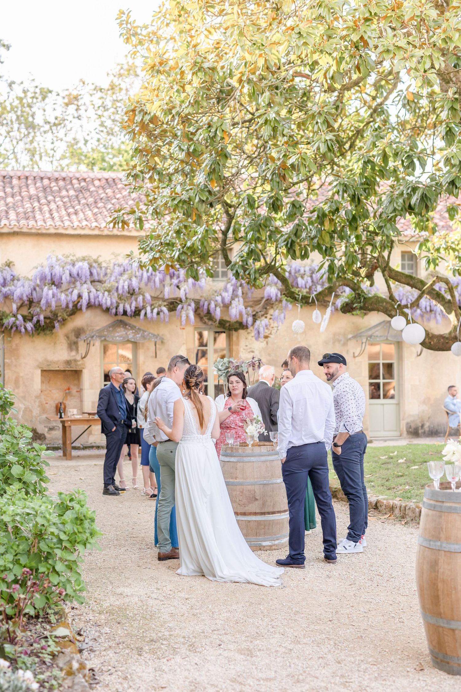Outdoor wedding reception with wisteria and wine barrels in rustic courtyard setting.