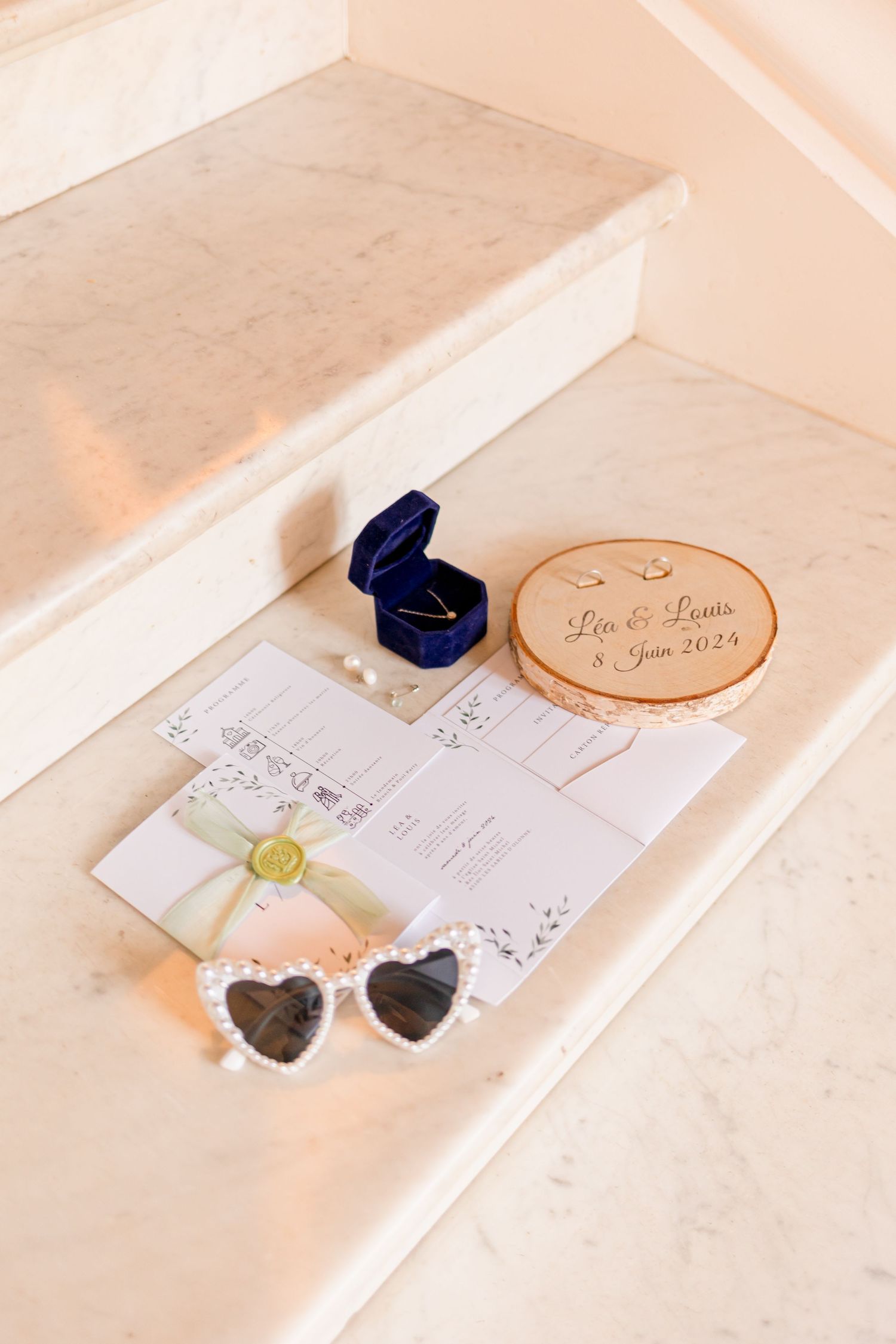 Wedding details including heart sunglasses, blue ring box and wooden decor on white steps.