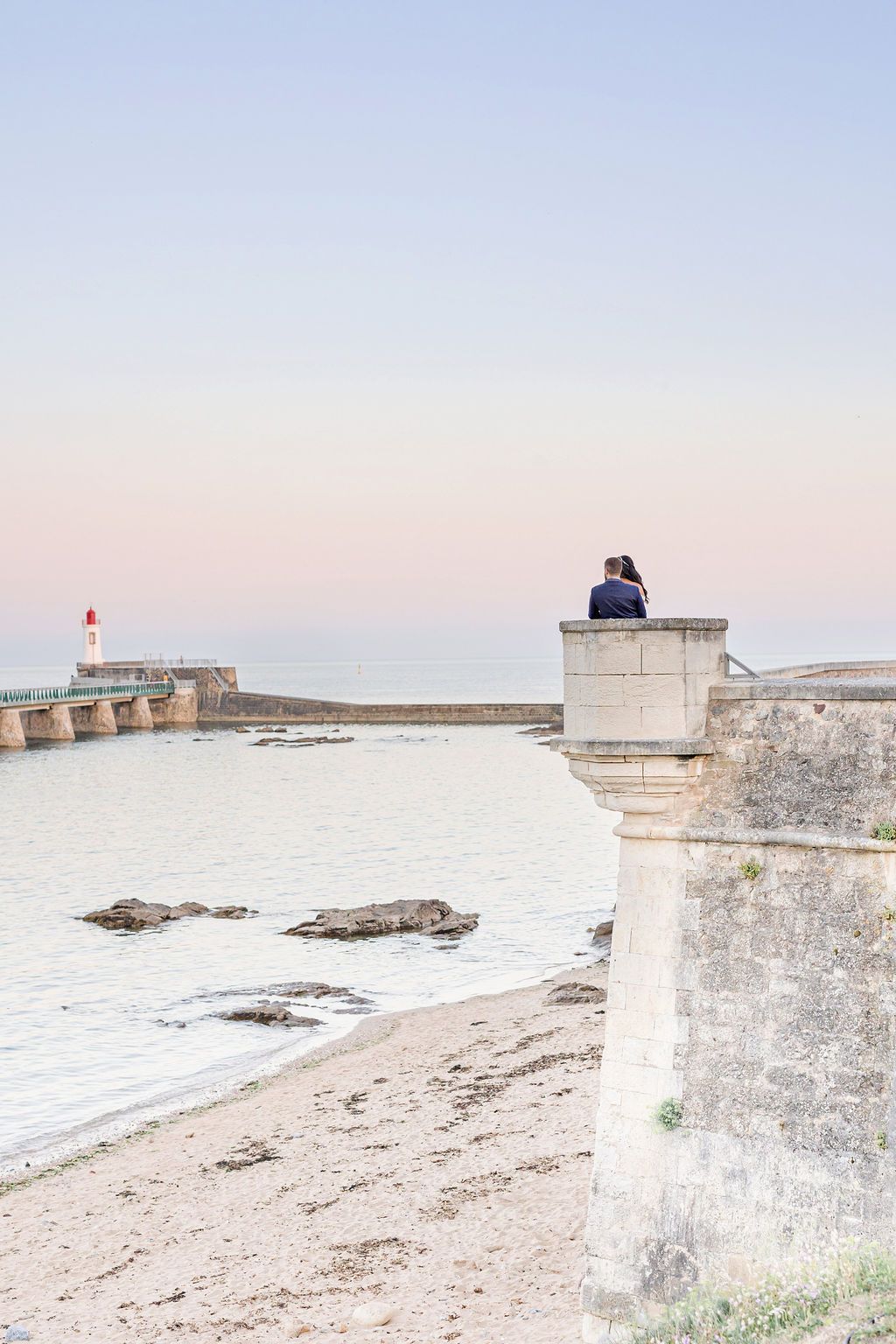 A stone pillar overlooking a coastal landscape with a lighthouse in the distance.